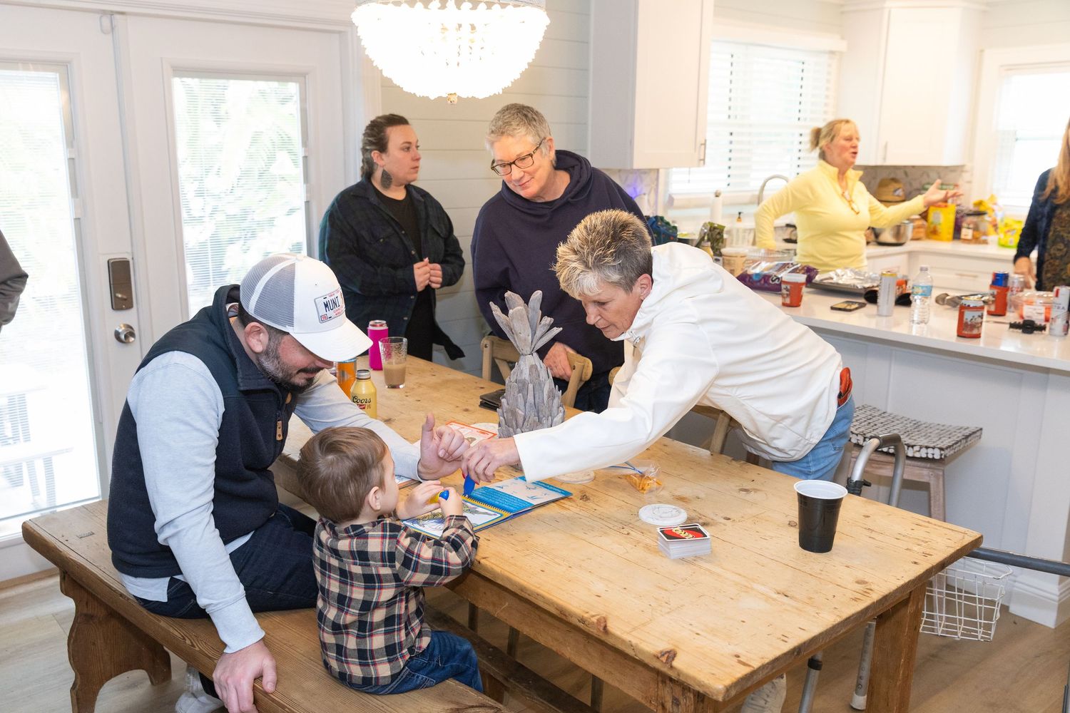 Family gathered around kitchen table as adults help young child with activity in modern home.