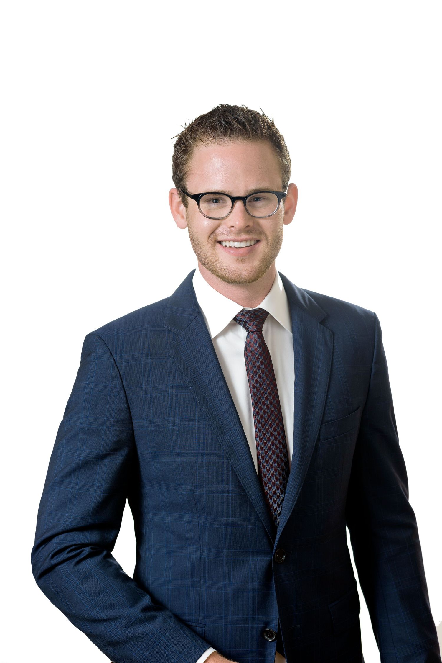 Young professional man in navy suit and glasses smiling confidently against white background.