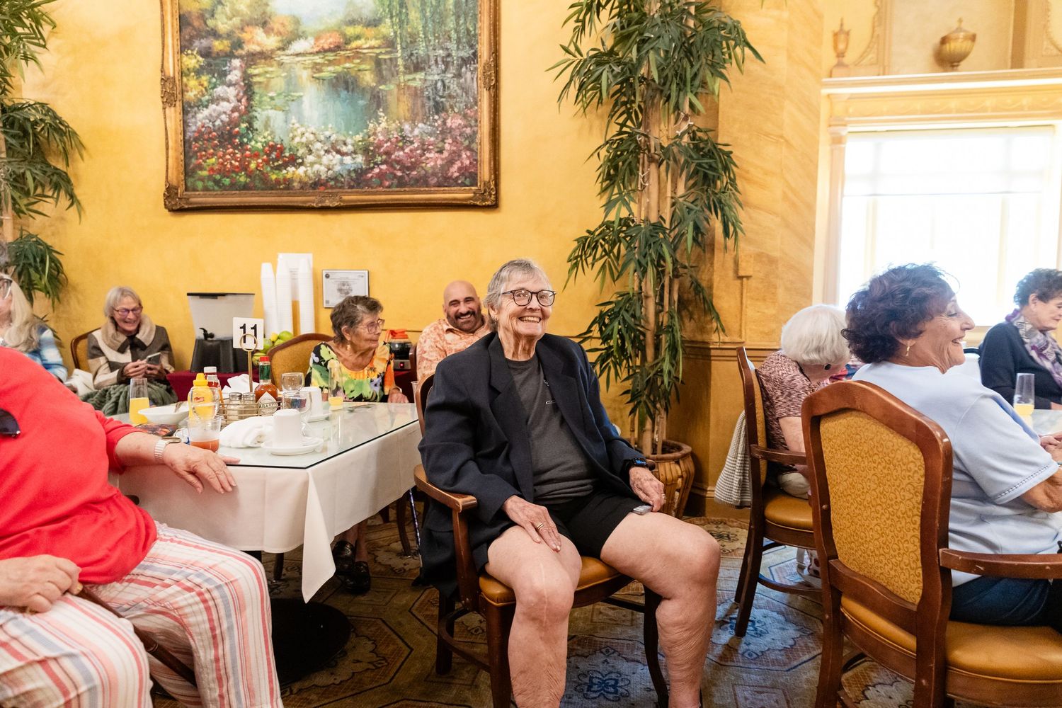 Group of seniors laughing and socializing at tables in a warmly decorated restaurant dining room.