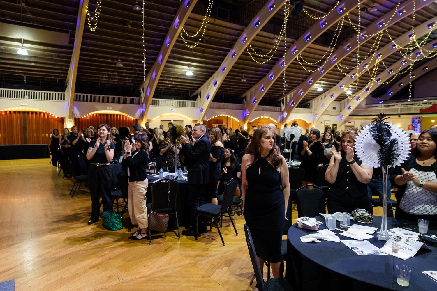 Crowd of elegantly dressed guests applauding at a casino-themed gala in a decorated ballroom.
