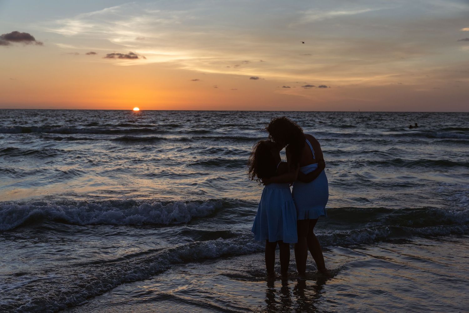 Couple embracing on beach shore at stunning orange sunset over ocean waves.