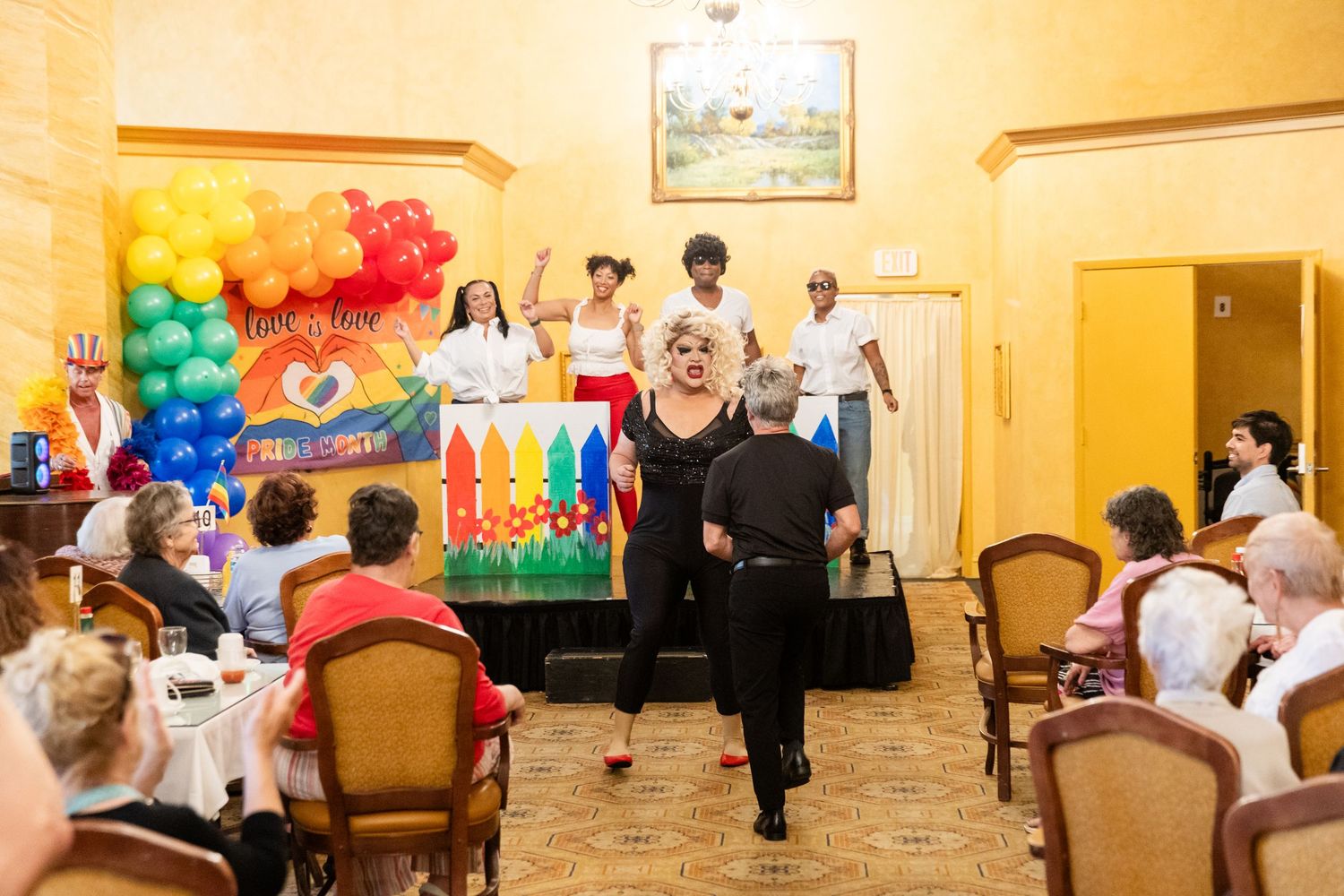 Colorful Pride event with drag performers and rainbow balloon decorations entertaining seated guests in a festive banquet hall.
