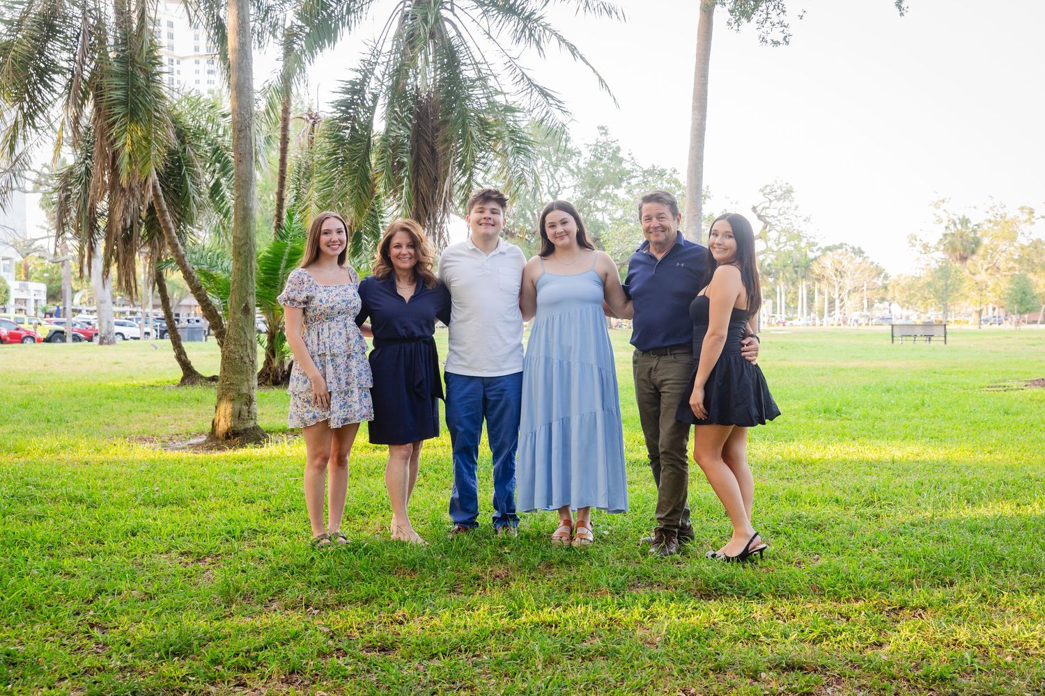 Happy family of six posing together in a tropical park surrounded by palm trees on a sunny day.