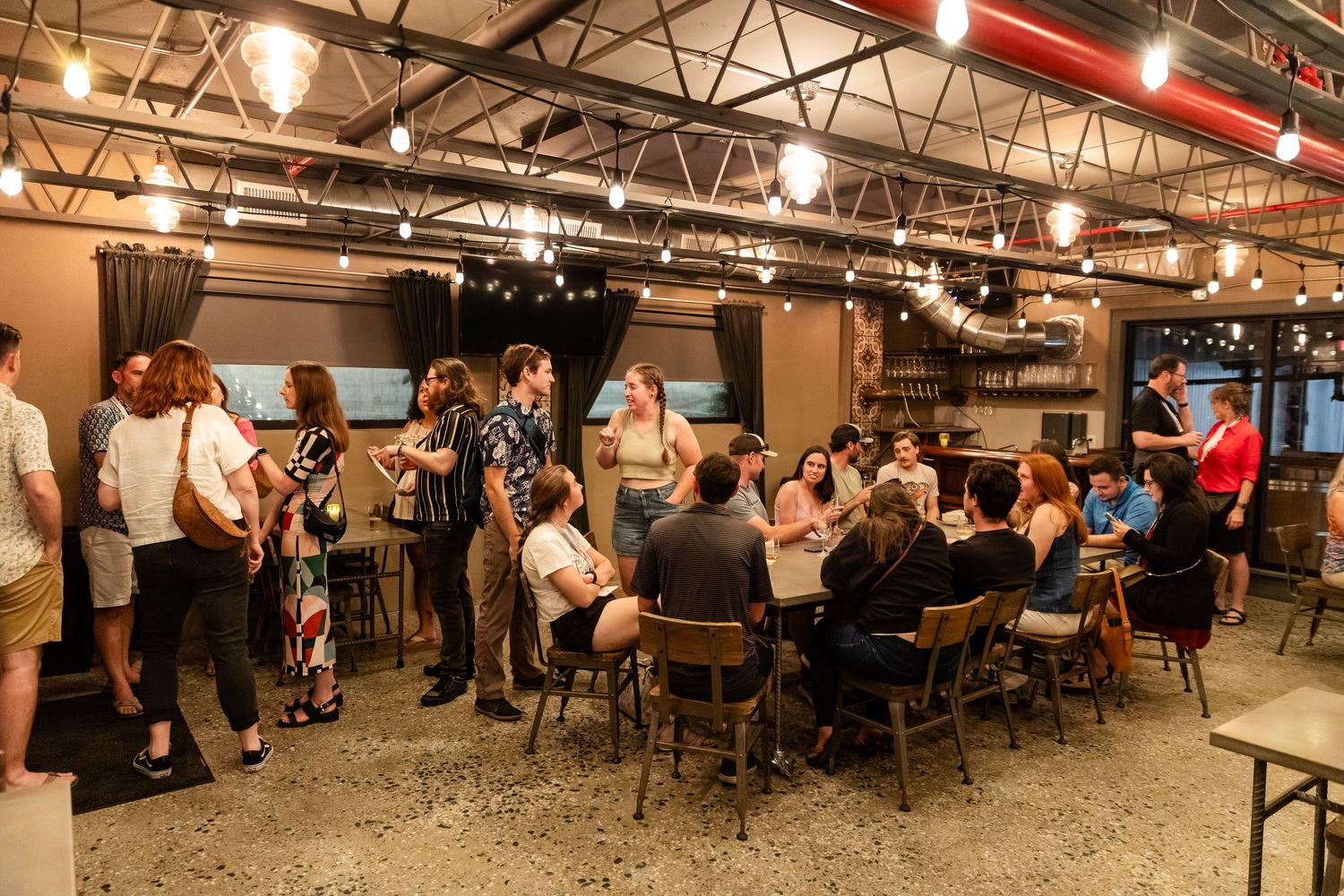 Groups of people socialize and sit at tables during an indoor evening networking event.