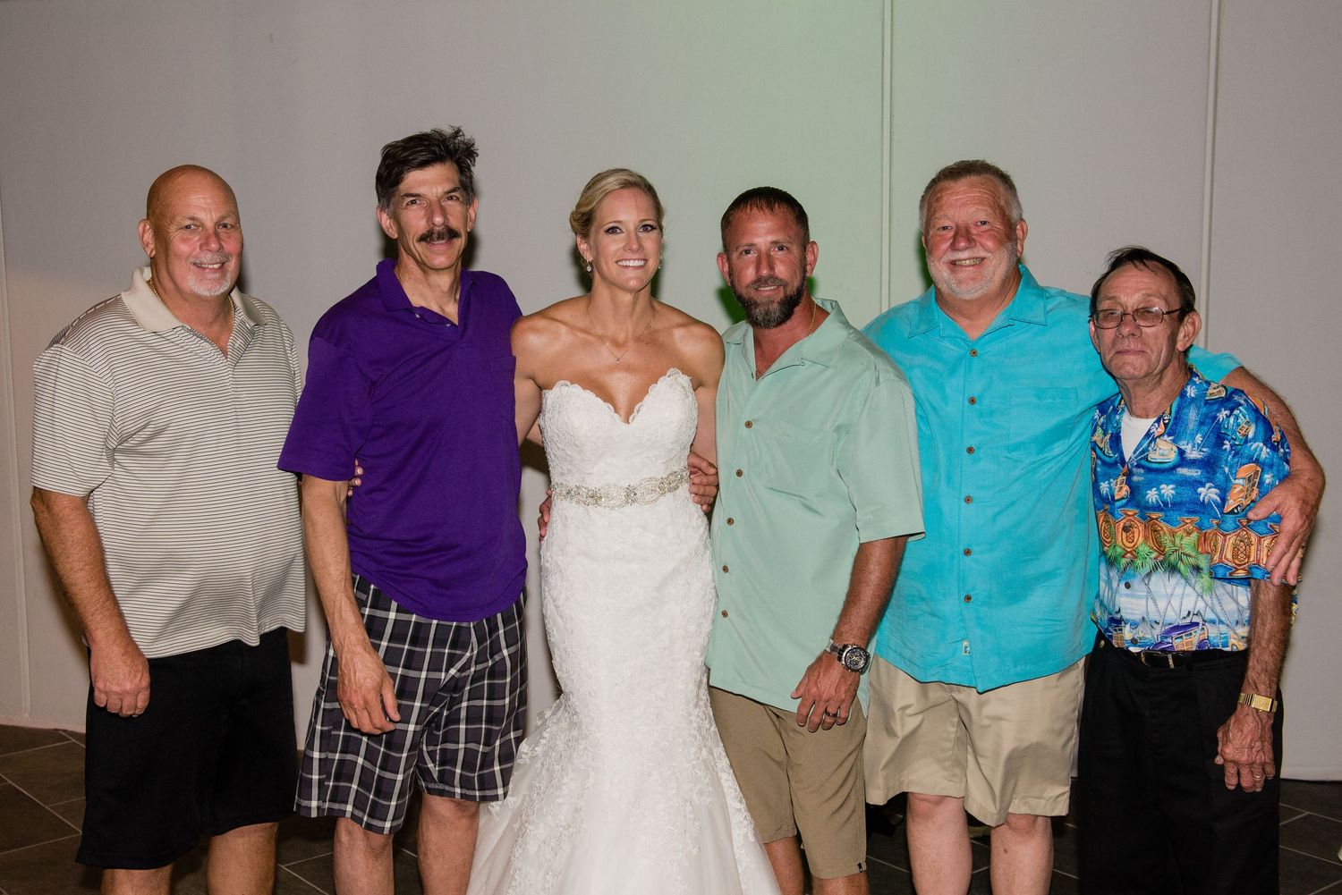 Bride in white wedding gown posing with five guests at a wedding reception celebration indoors.