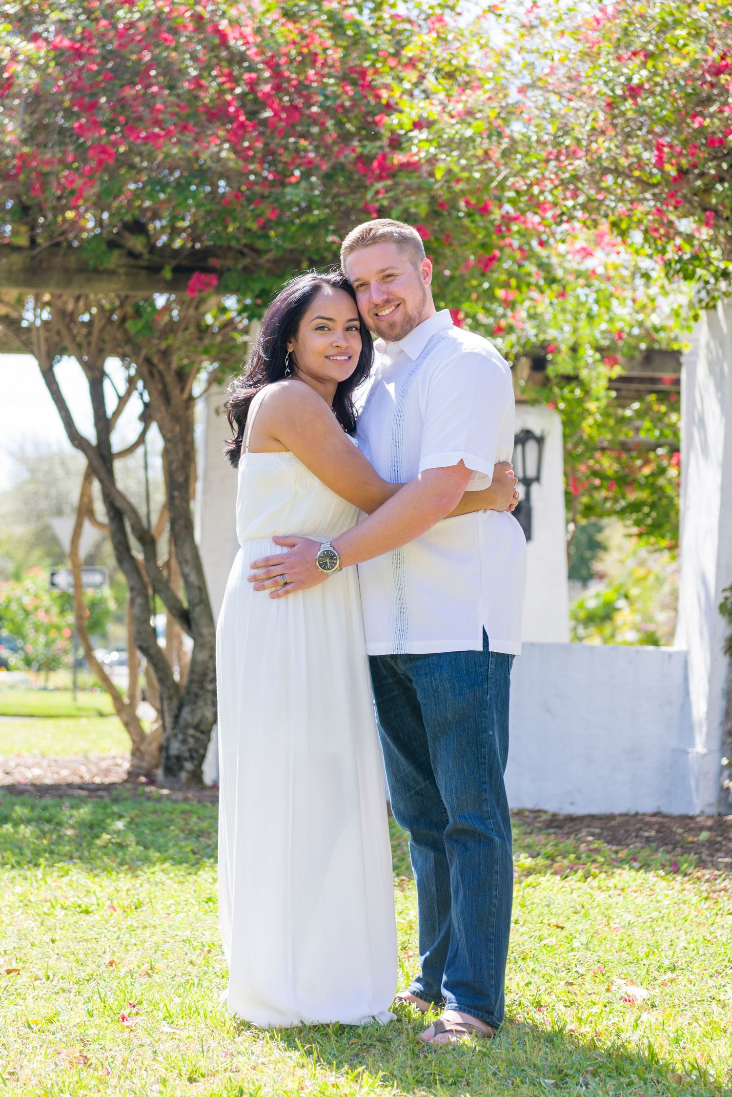 Happy interracial couple embracing and smiling outdoors under vibrant pink flowering bougainvillea trees.