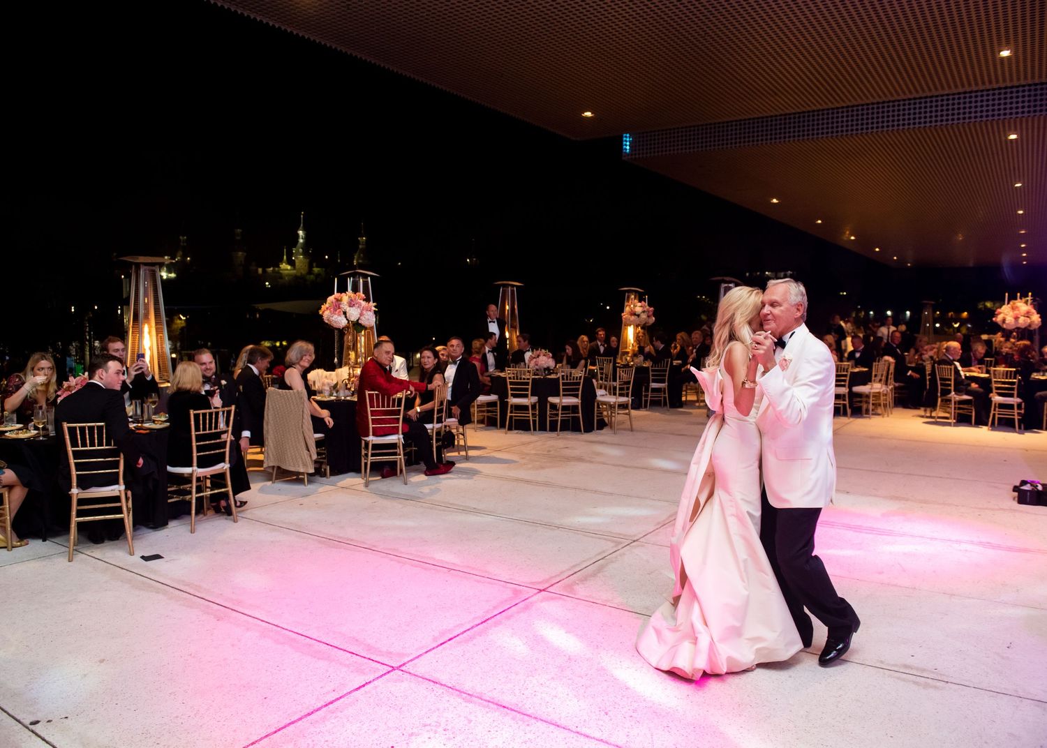 Couple shares romantic wedding dance on illuminated floor with guests seated at decorated tables.