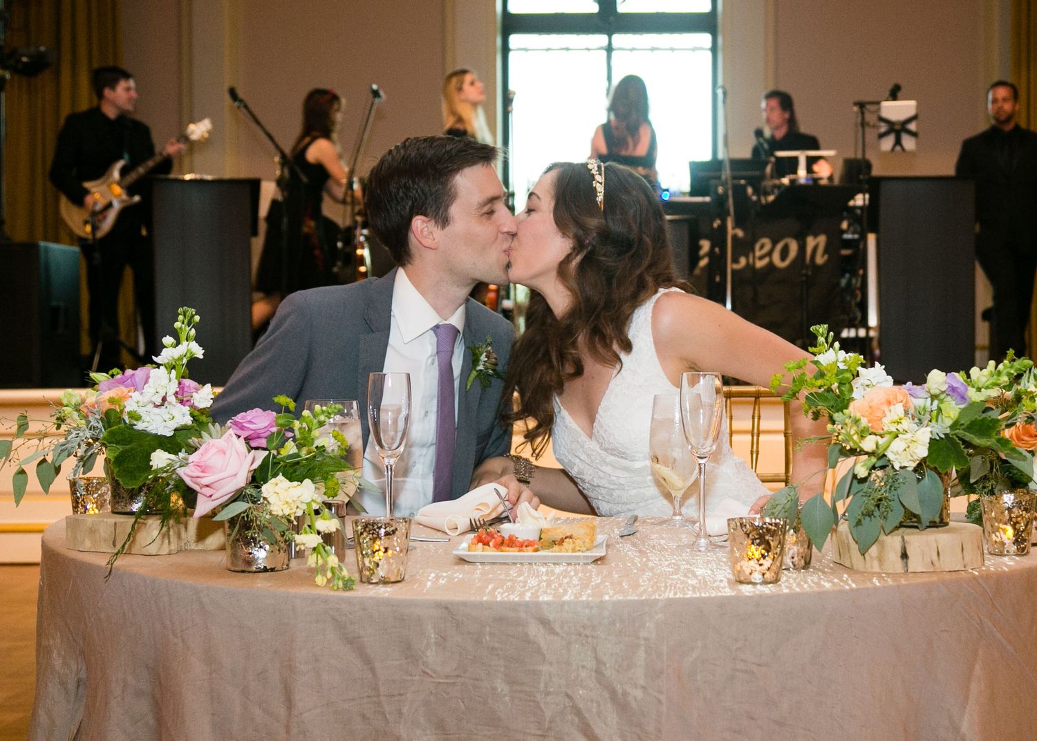 Bride and groom sharing a kiss at sweetheart table with live band.