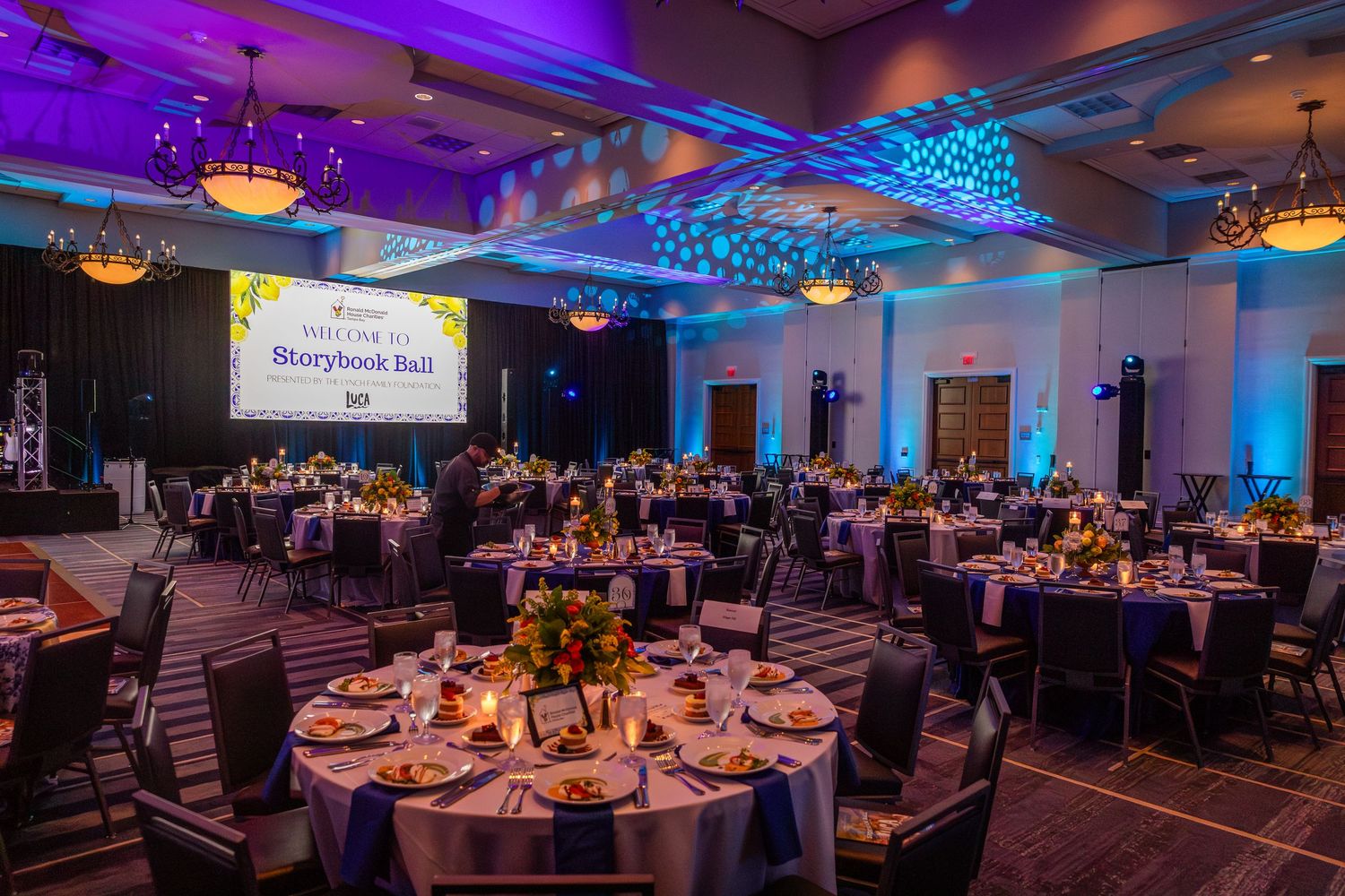 Elegant ballroom event setup with round tables, purple lighting, and a Storybook Ball banner for a formal gala dinner.