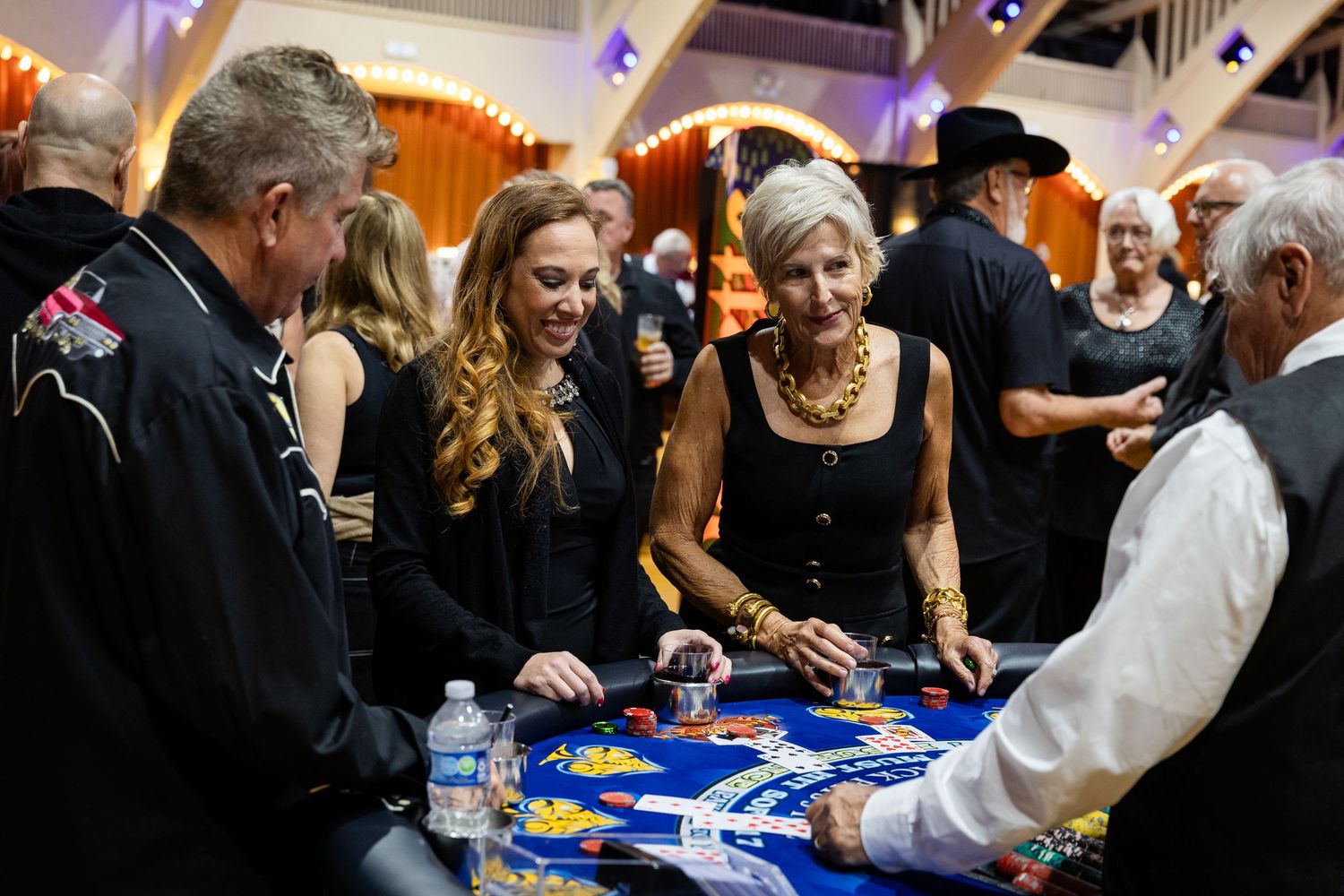 Guests enjoy a casino night fundraiser event, playing cards at a blackjack table in an elegant venue.
