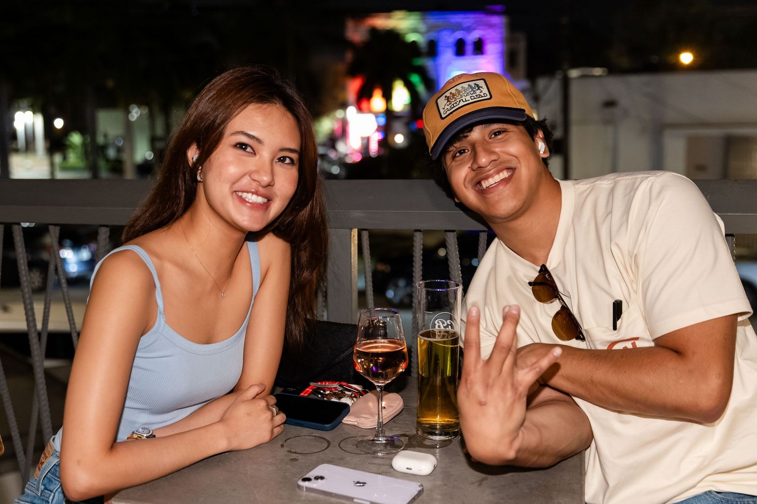 A smiling couple sits at an outdoor bar table at night with drinks.