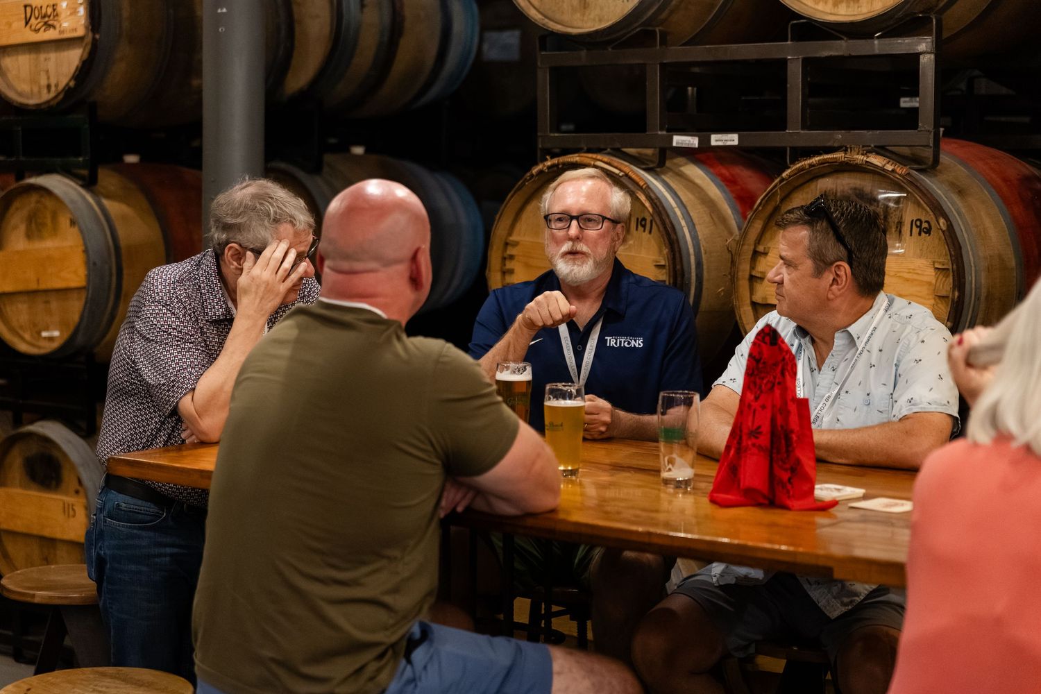 Men socializing at a brewery tasting room with wooden barrels in the background, enjoying craft beer together.