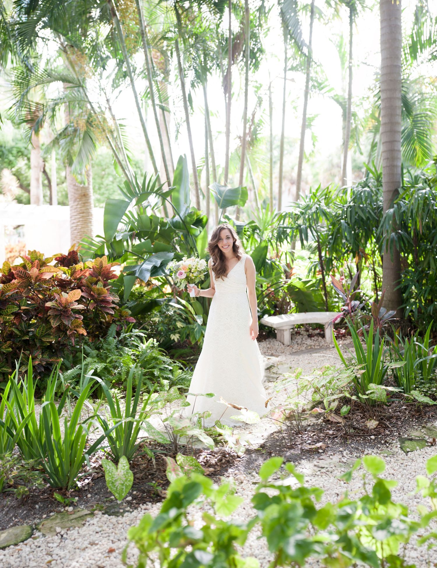 Bride in white gown stands in lush tropical garden surrounded by palm trees and colorful foliage in the Vinoy Resort St. Petersburg.