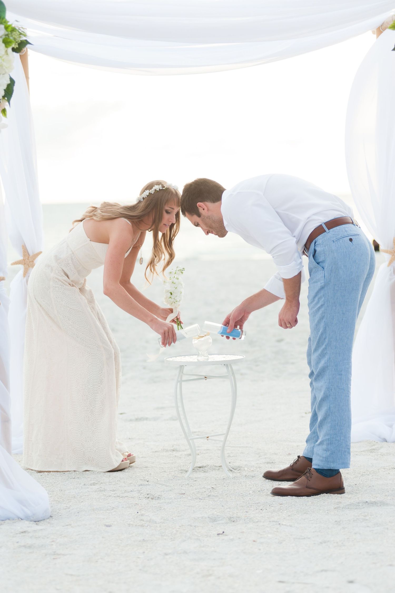 Bride and groom perform sand ceremony at small white table during beach wedding on Treasure Island, Florida.