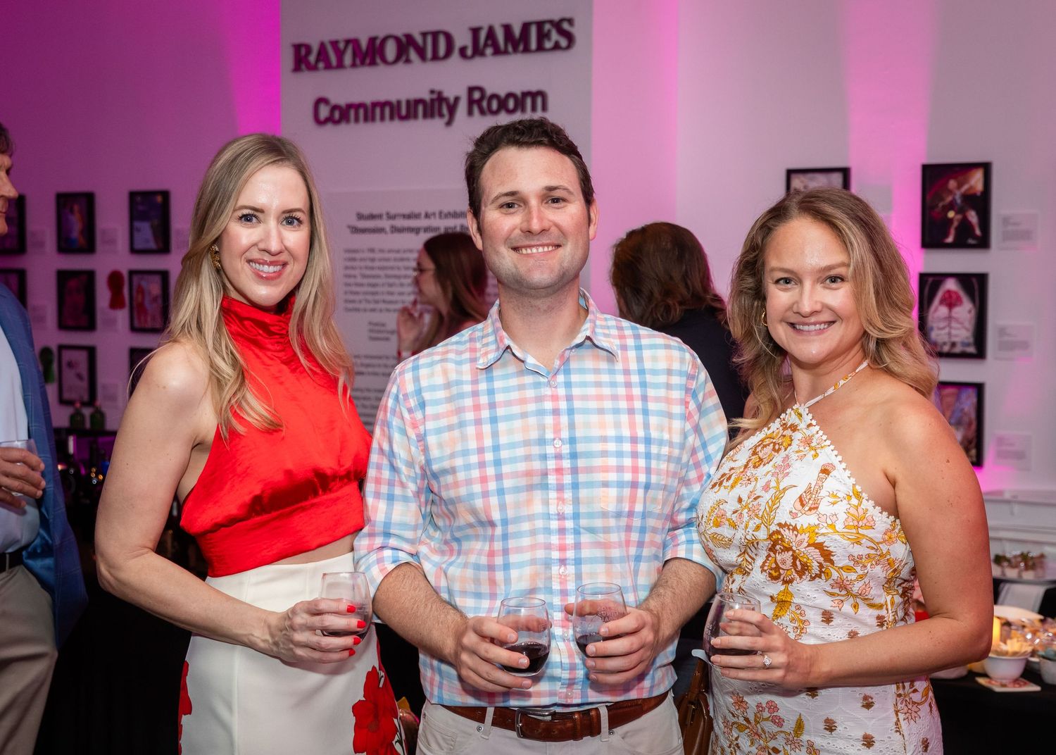 Three smiling guests pose with drinks at a Raymond James Community Room social event.