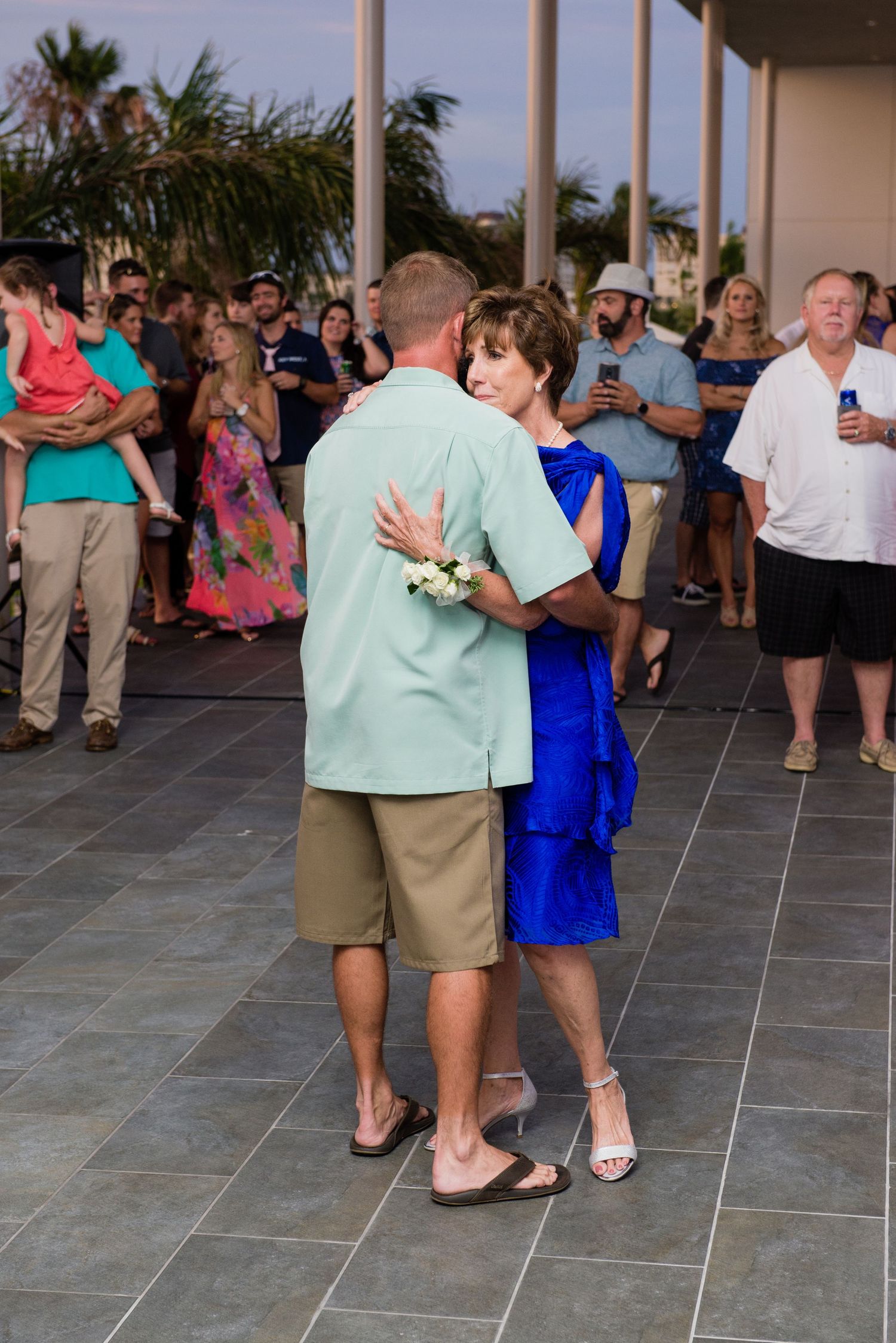 Mother and son share a dance at outdoor wedding reception with guests watching.