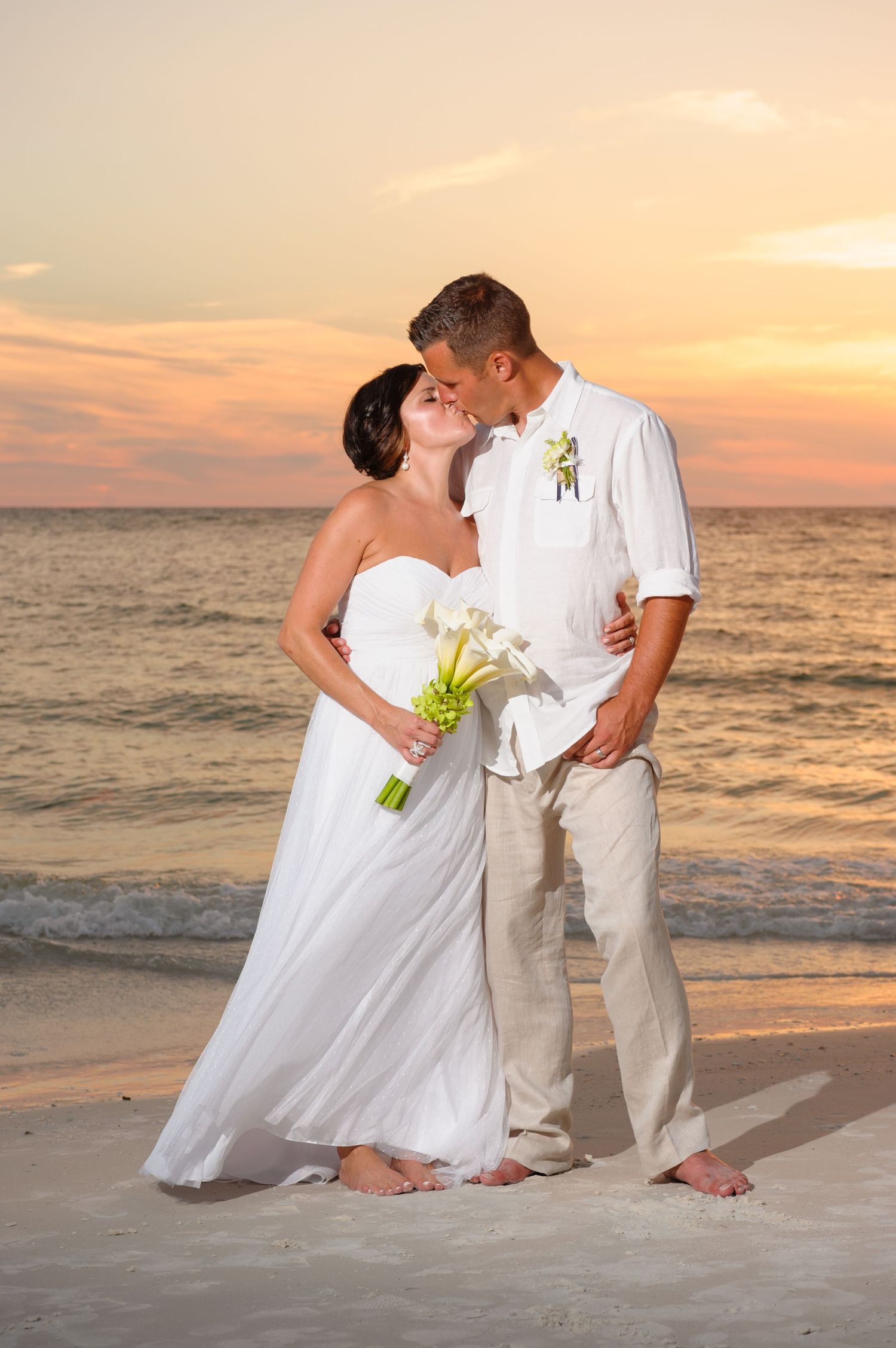 Bride and groom sharing a romantic kiss on the beach at a stunning golden sunset.