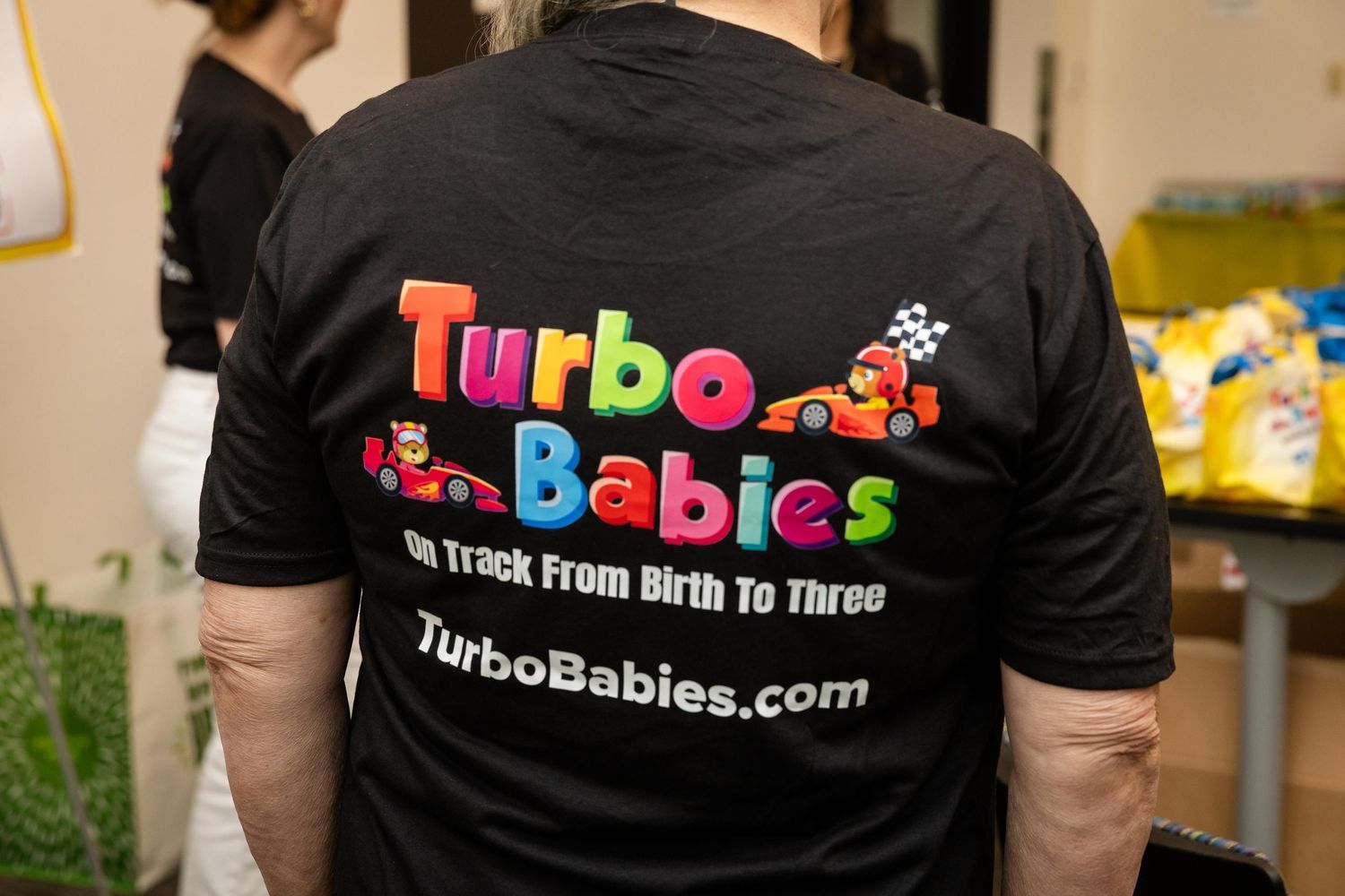 Person wearing a black Turbo Babies t-shirt promoting TurboBabies.com, a child development program for birth to three.