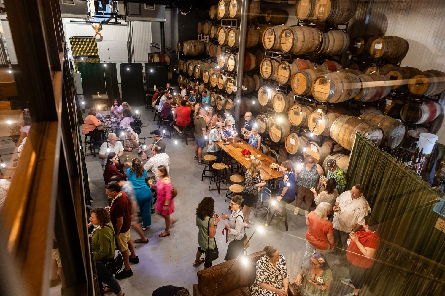 Guests mingle inside a rustic winery barrel room with wooden barrels lining the walls during a lively evening event.