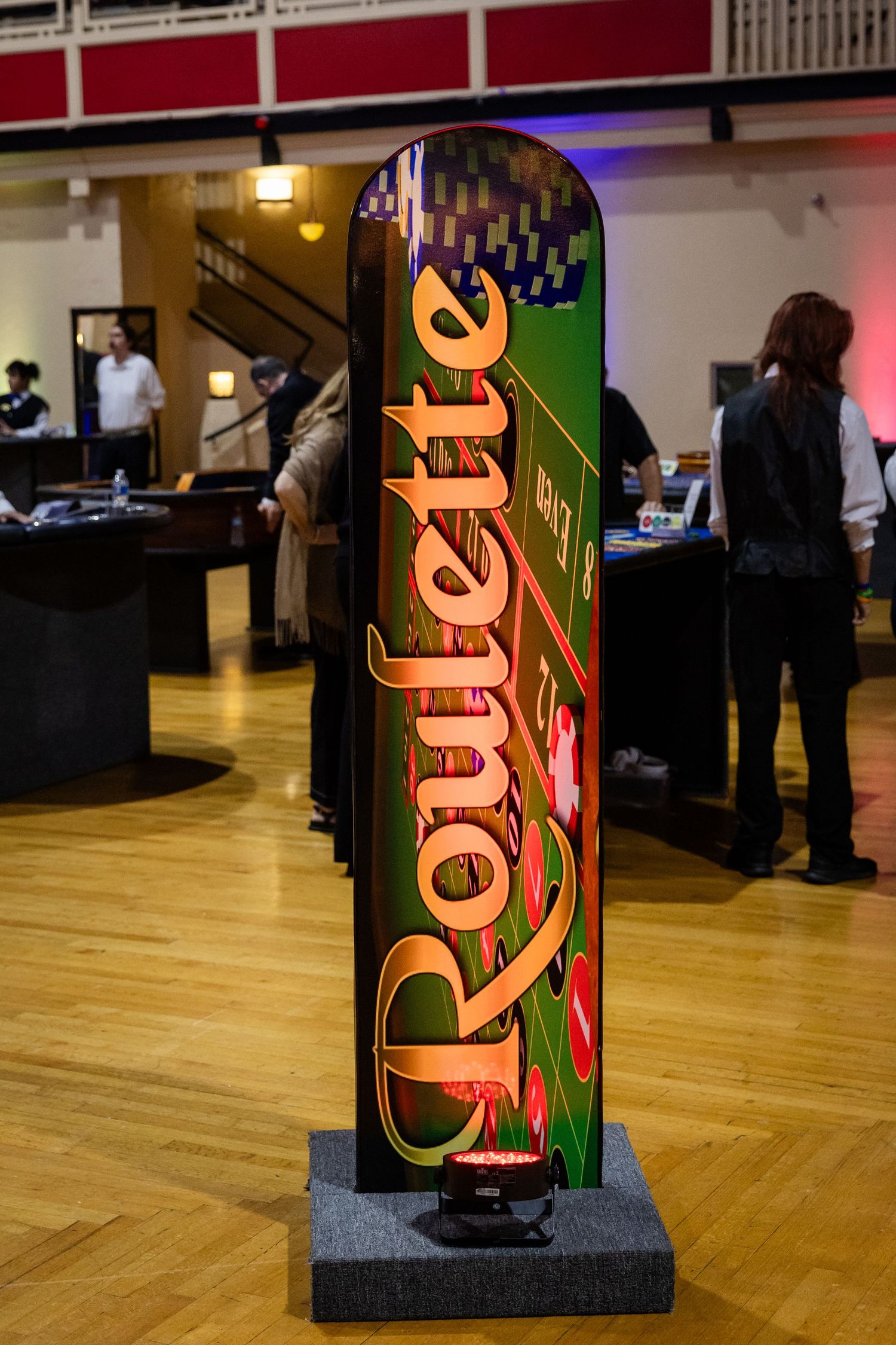 Colorful illuminated Roulette sign standing on a wooden floor at a casino night event.