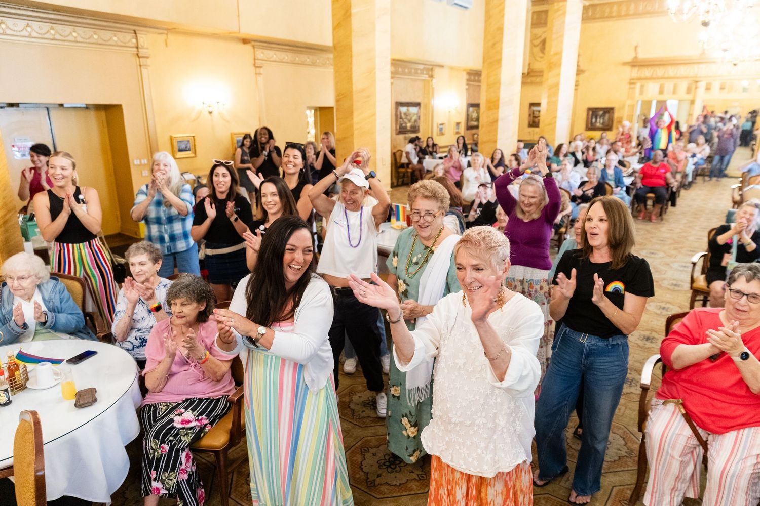 Large group of diverse women clapping and dancing joyfully at a community celebration event indoors.