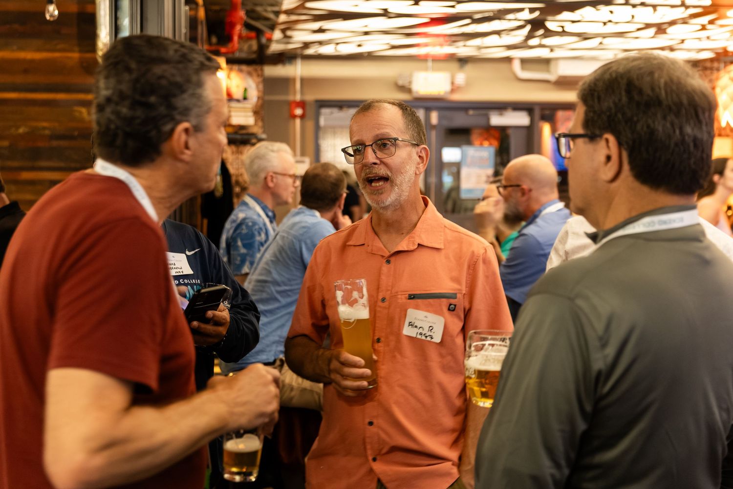 Three men socializing and drinking beer at an indoor brewery gathering event.