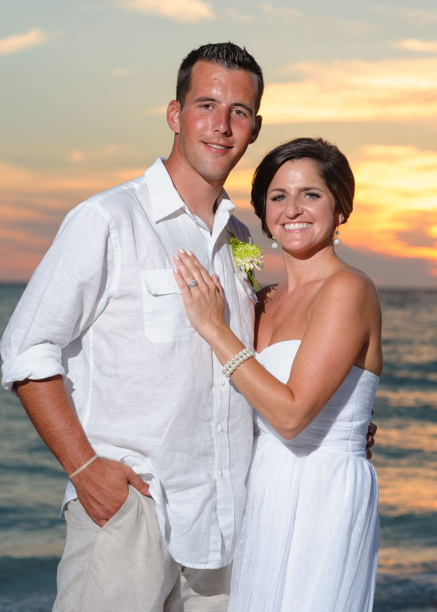 Happy bride and groom portrait on the beach with a glowing orange sunset behind them.