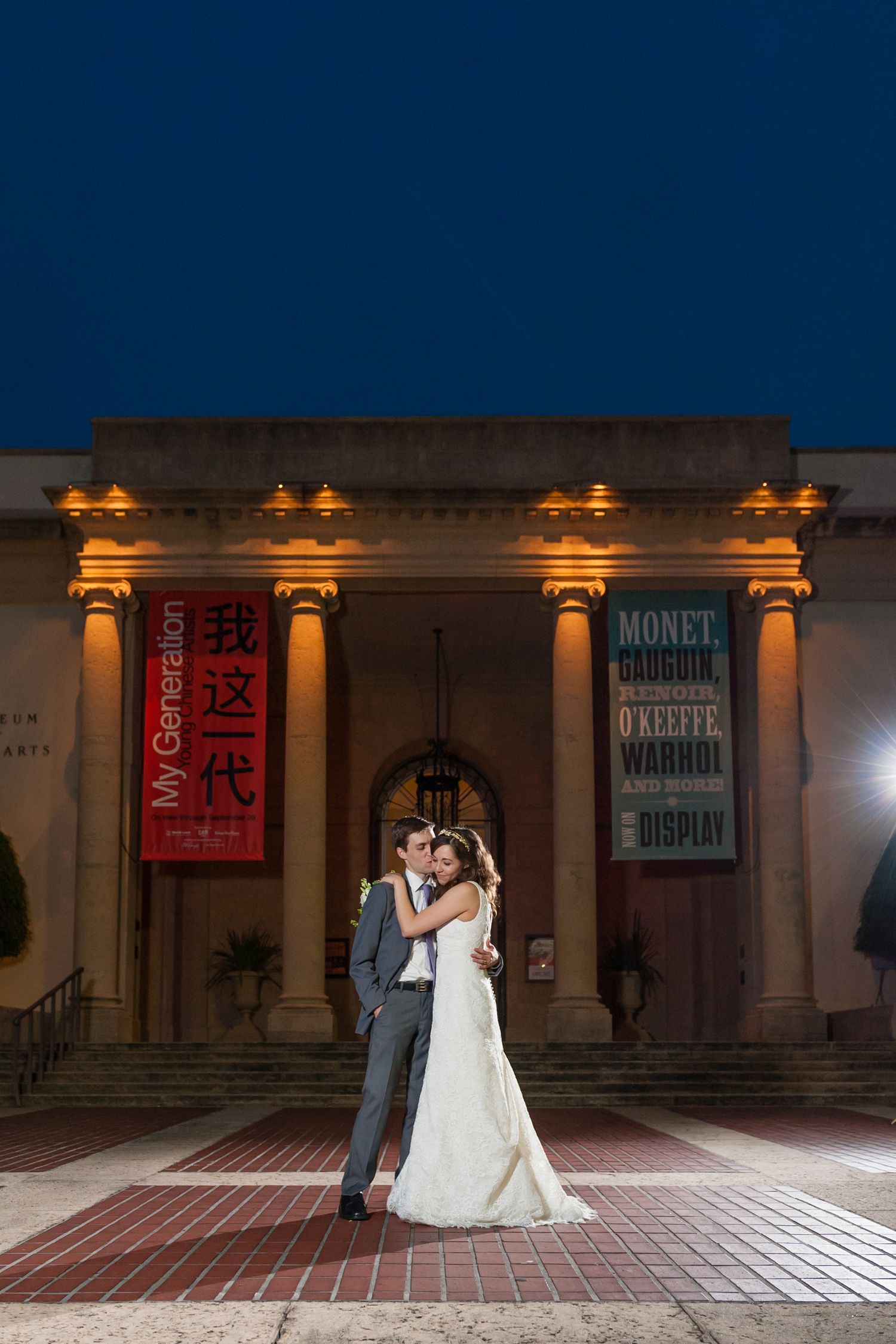 Bride and groom embrace outside illuminated museum at night.