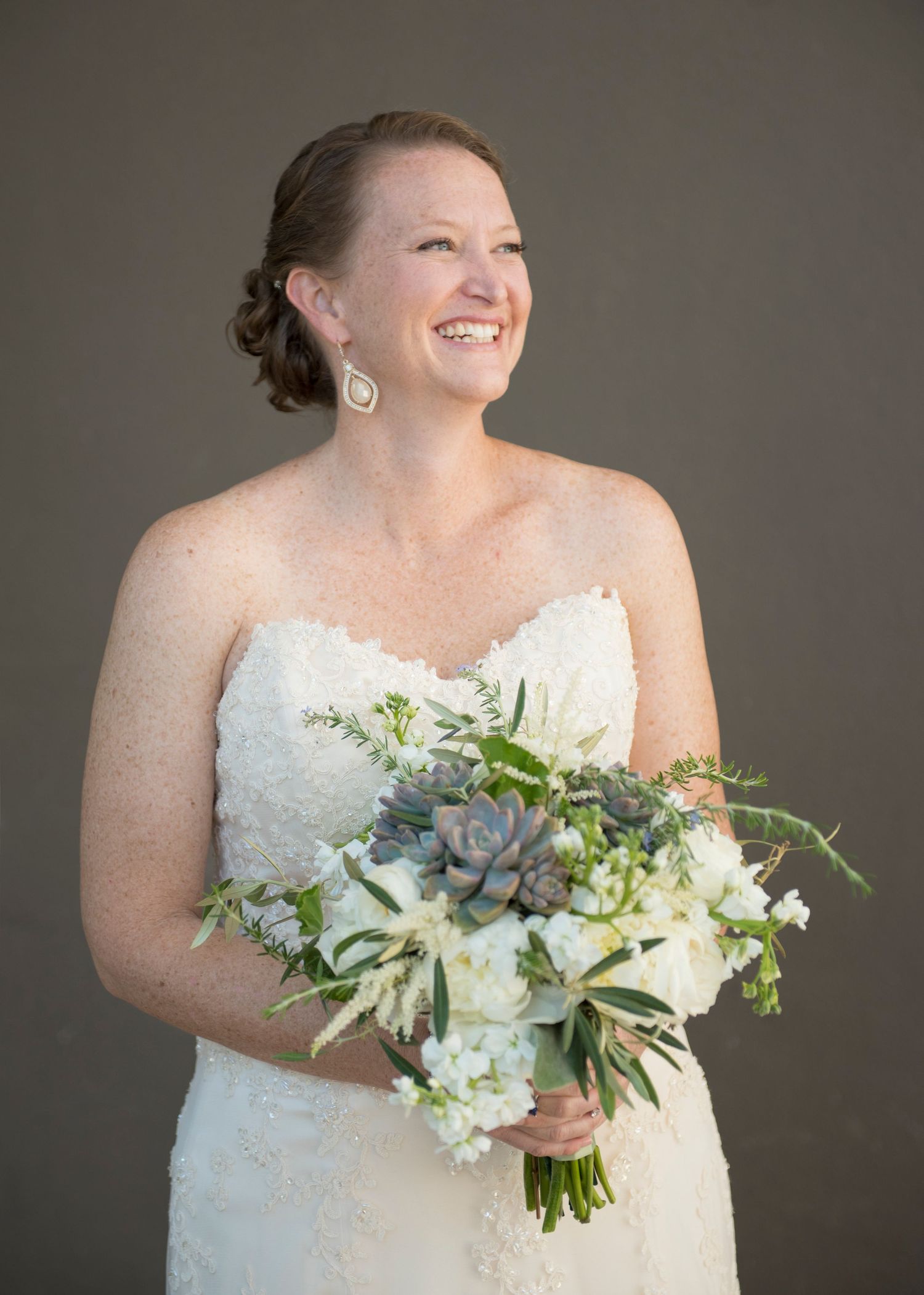 Smiling bride in strapless lace wedding gown holding elegant bouquet of white flowers and succulents St. Petersburg.