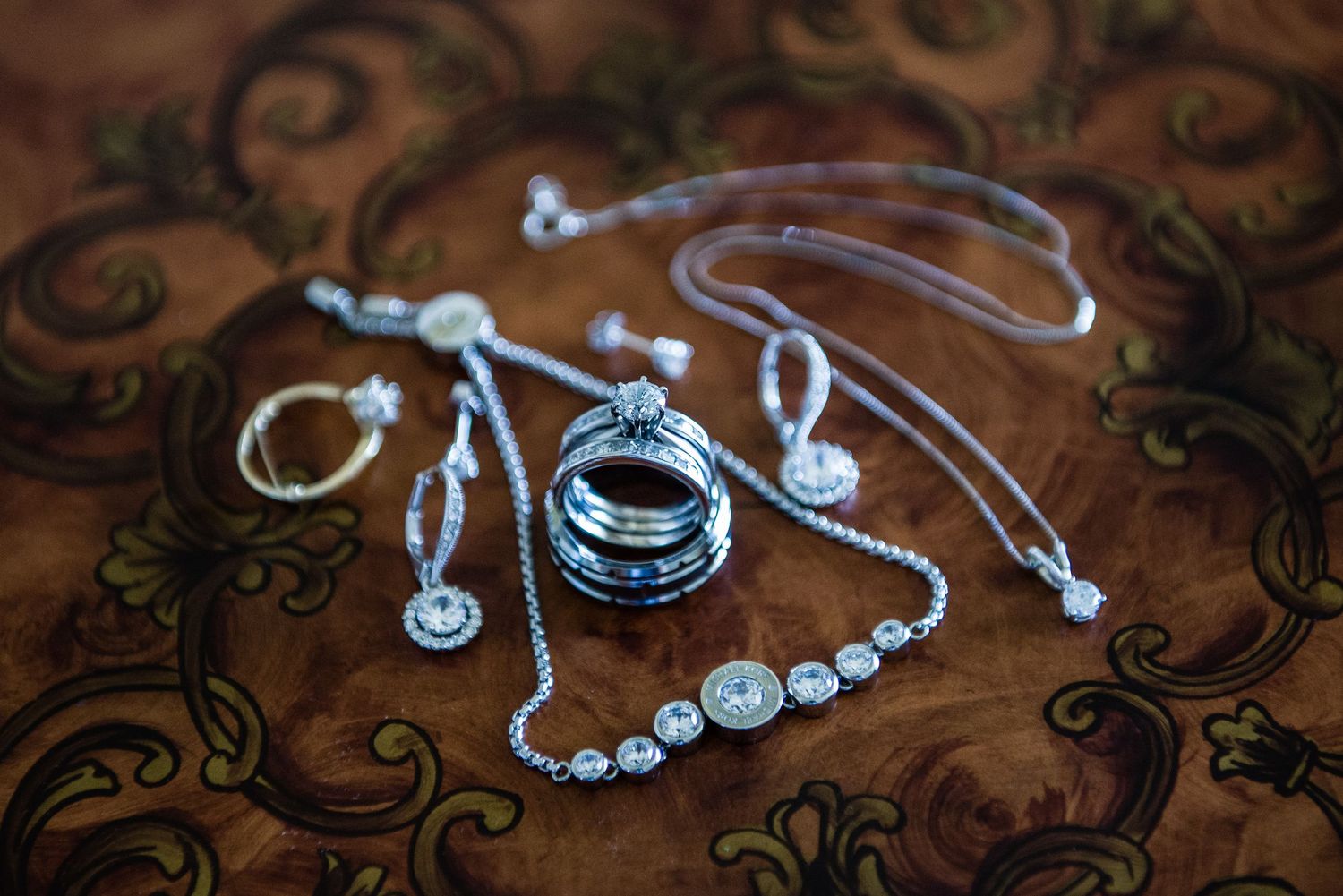Elegant silver diamond jewelry set including rings, necklaces, and earrings on ornate surface.