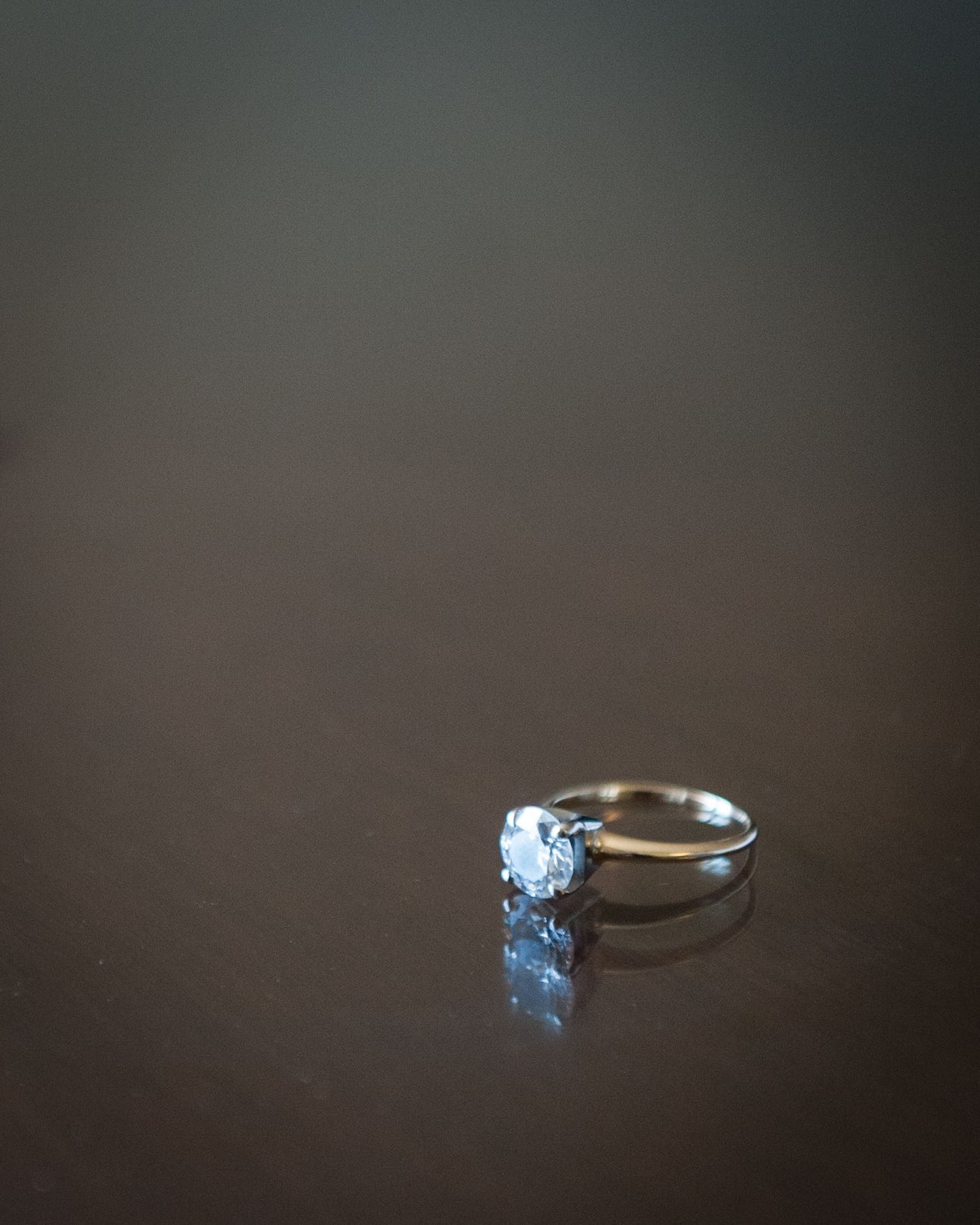 A silver solitaire diamond engagement ring resting on a dark reflective surface.