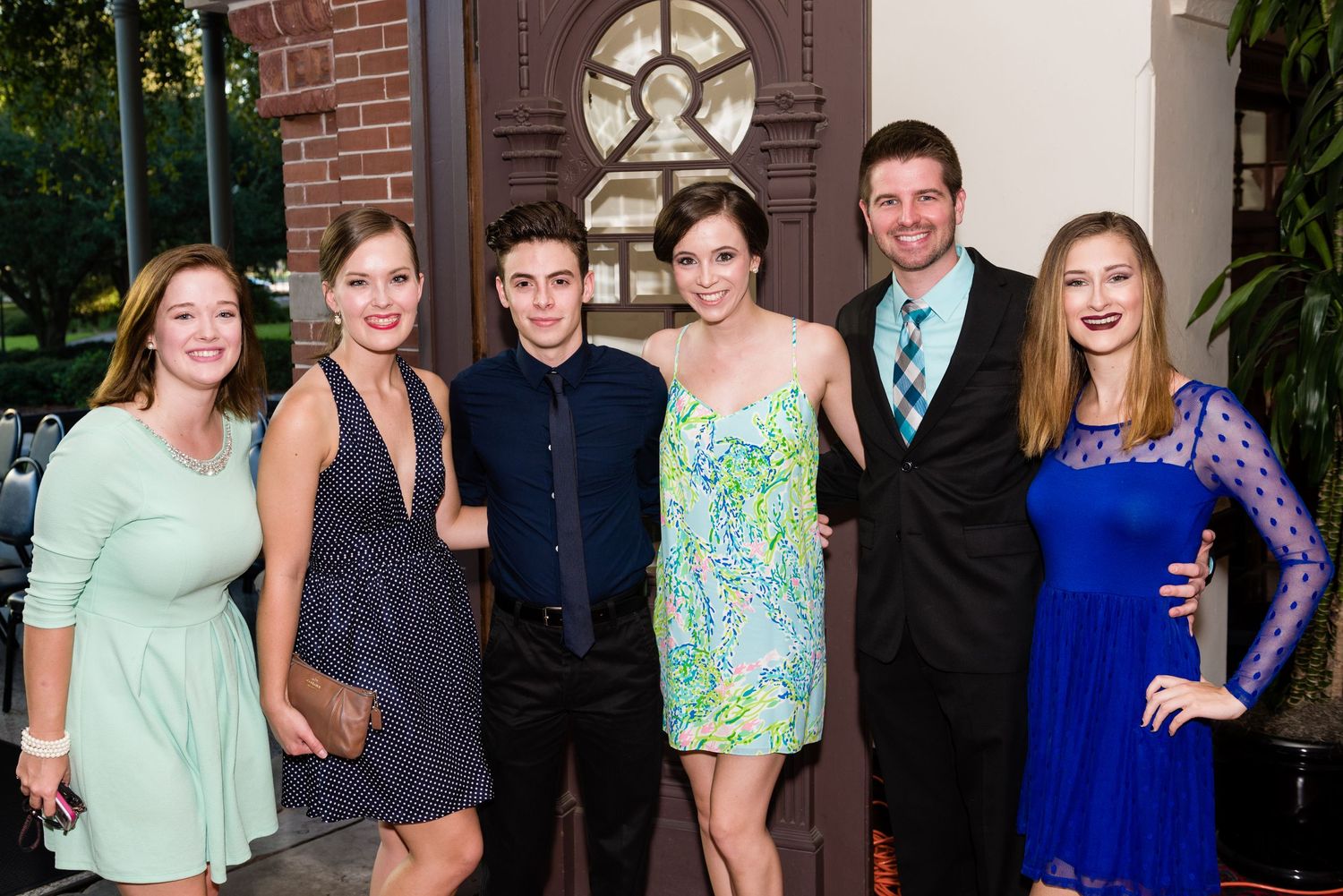 Six young adults dressed in formal attire posing together outdoors at an evening event.