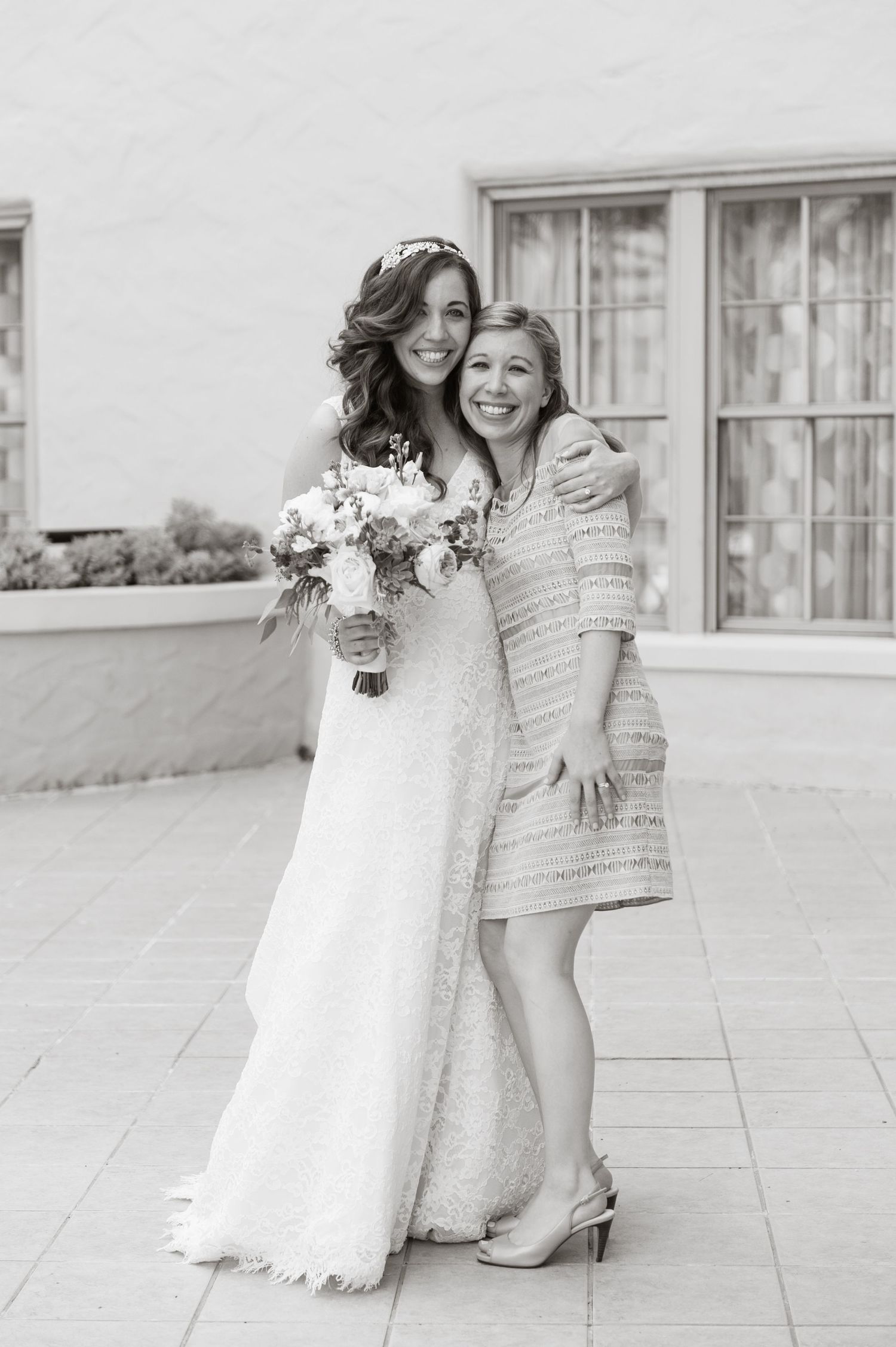 Black and white photo of bride in lace gown hugging smiling woman in short dress outdoors at The Vinoy Resort.