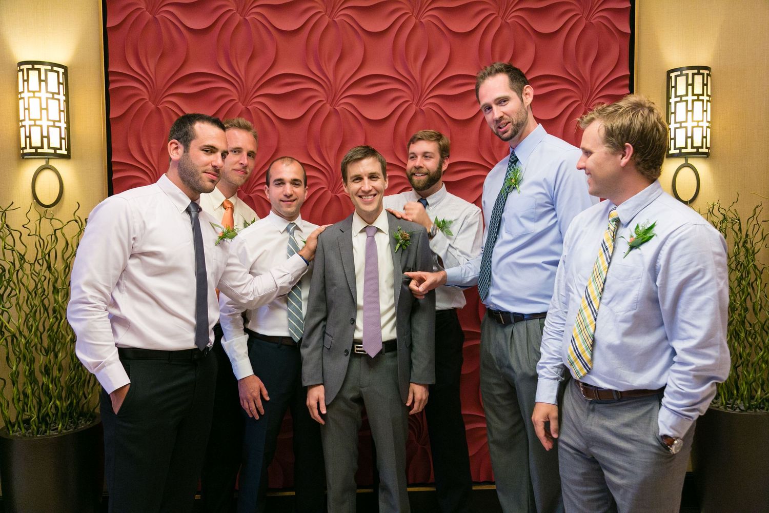 Groom poses with groomsmen in gray and navy suits with colorful ties and boutonnieres at wedding reception.