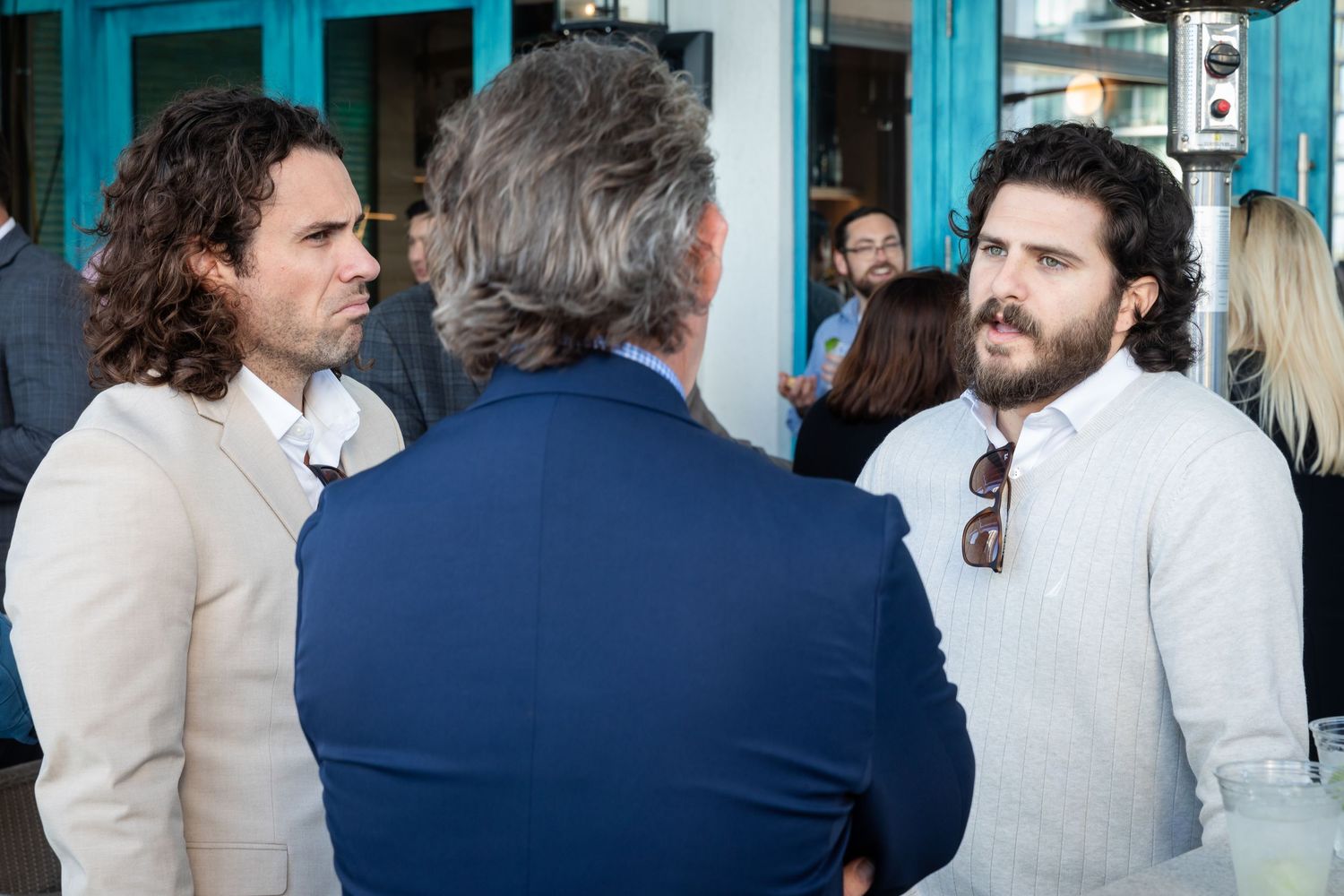 Three men in business casual attire engaged in conversation at an outdoor networking event.