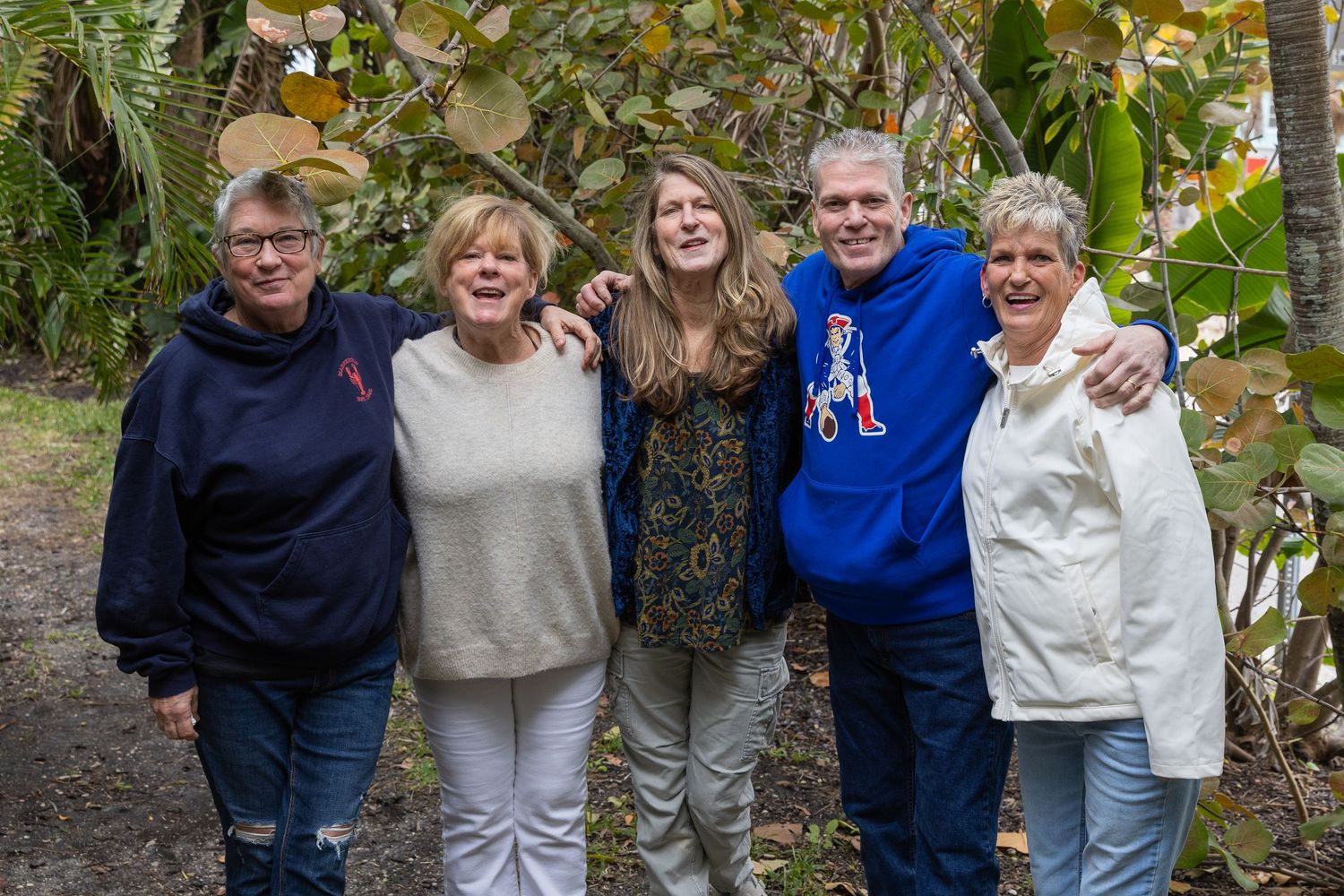 Five adults smiling together outdoors in a lush garden setting, posing for a group photo.