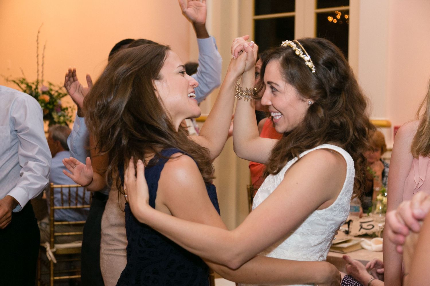 Bride and bridesmaid laugh and dance together joyfully at wedding reception celebration.