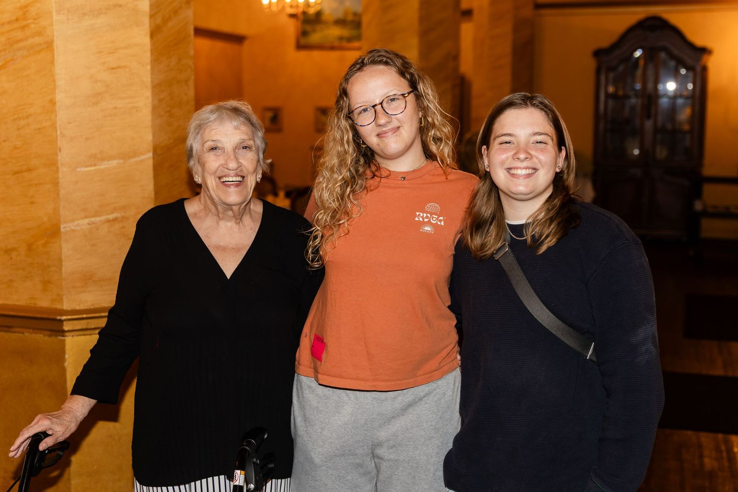 Three women of different generations smiling together at an elegant indoor community social event.