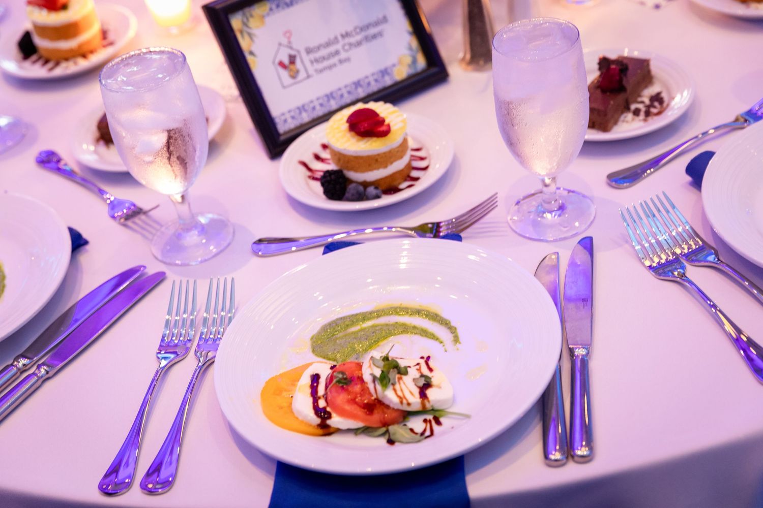 Elegant plated caprese salad appetizer at a formal dinner event with desserts and glassware in background.
