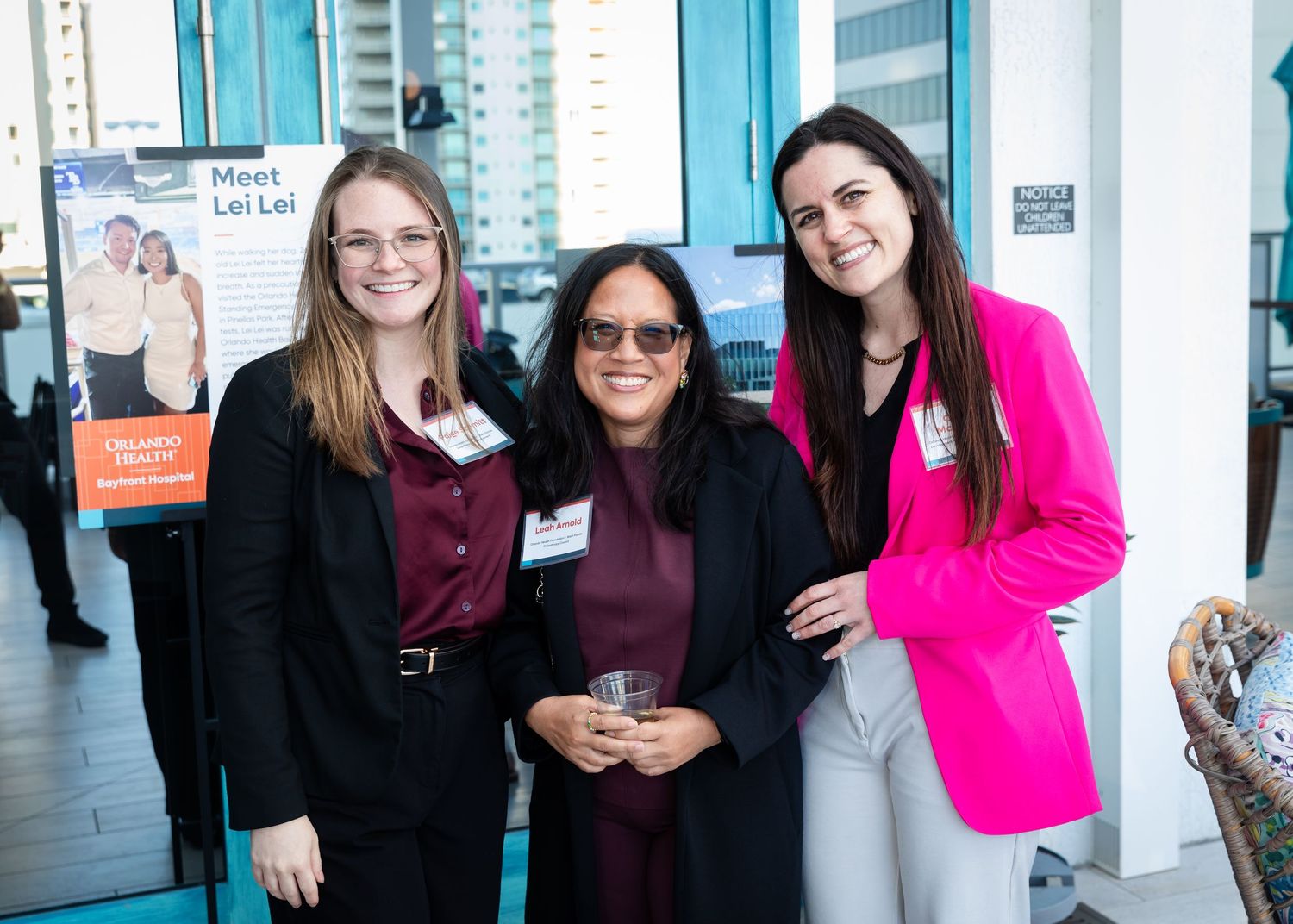 Three women smiling at a professional networking event near a Meet Lei Lei banner.