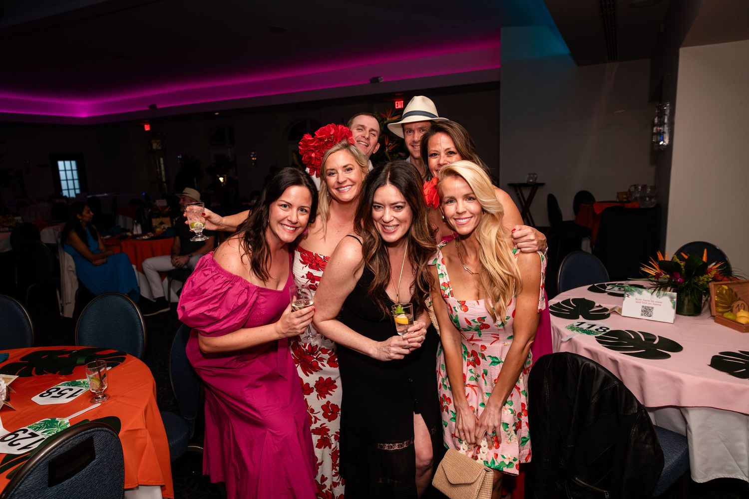 Group of women posing together at a festive indoor party event with colorful decorations and ambient lighting.