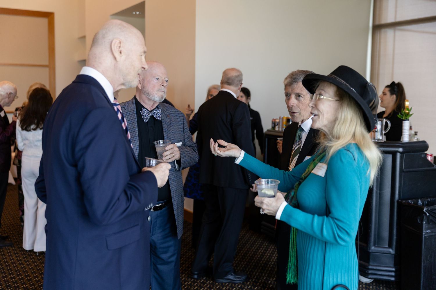 Professionals networking at a formal event, engaging in conversation while holding drinks in a conference room.
