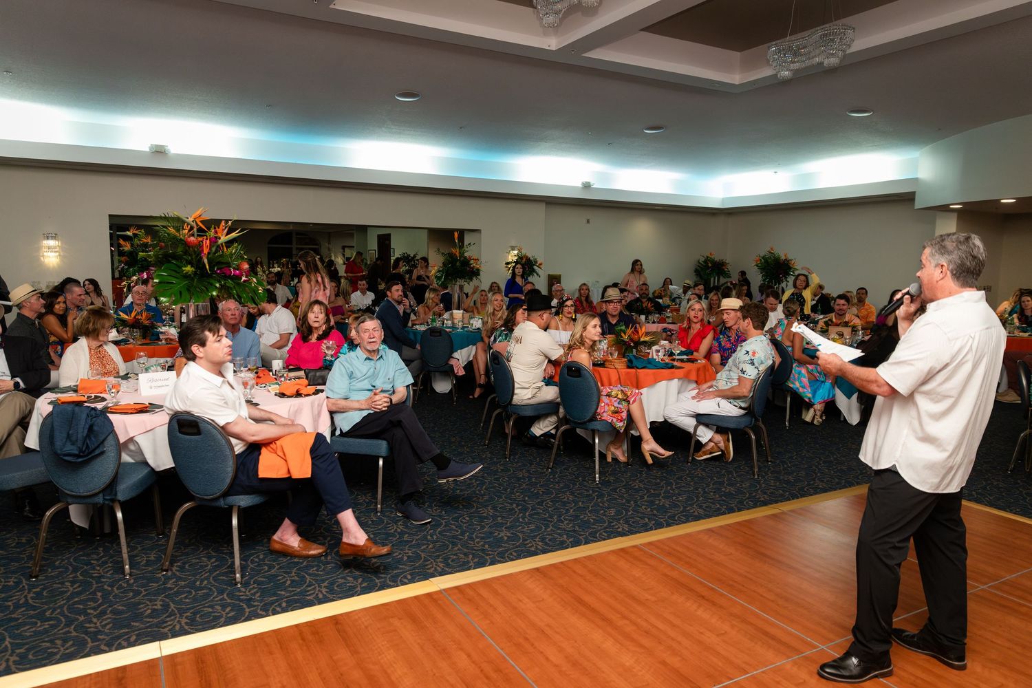 Speaker addresses a large audience at a corporate banquet event in a modern conference hall.