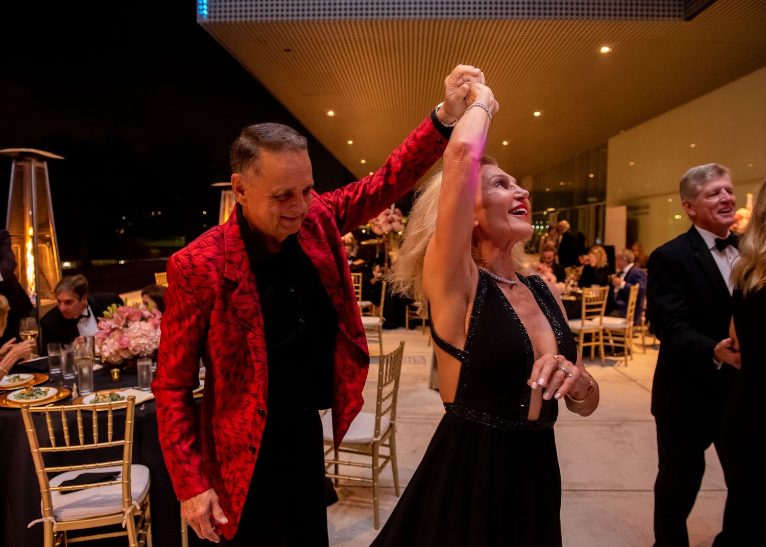 Couple dancing joyfully at wedding reception, man wearing bold red patterned blazer.
