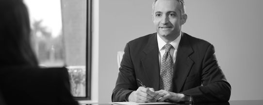 Professional businessman in suit sitting at desk during meeting, black and white corporate portrait photography.