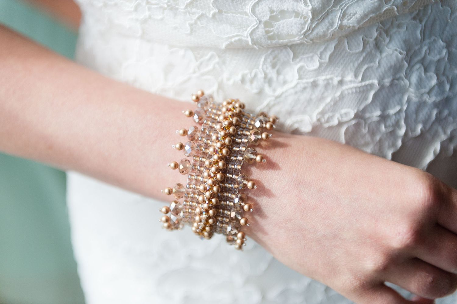 Close-up of a bride's wrist adorned with a sparkling layered gold and crystal beaded bracelet on lace gown.