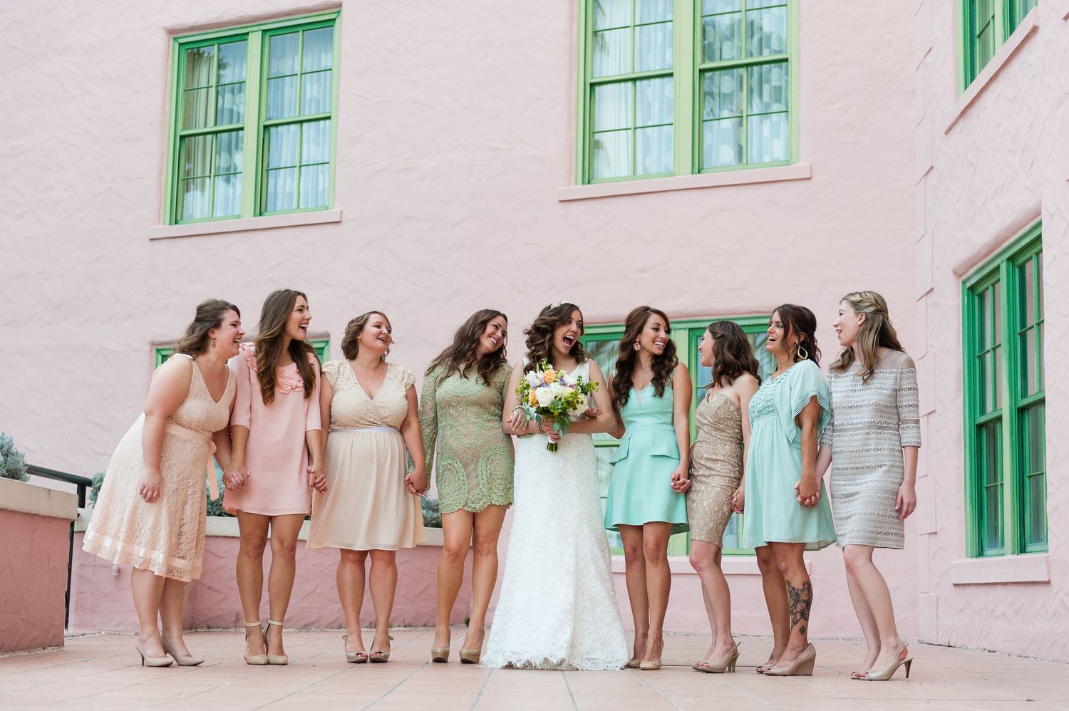Bride in white gown surrounded by bridesmaids in pastel dresses walking outside pink building at The Vinoy Resort.