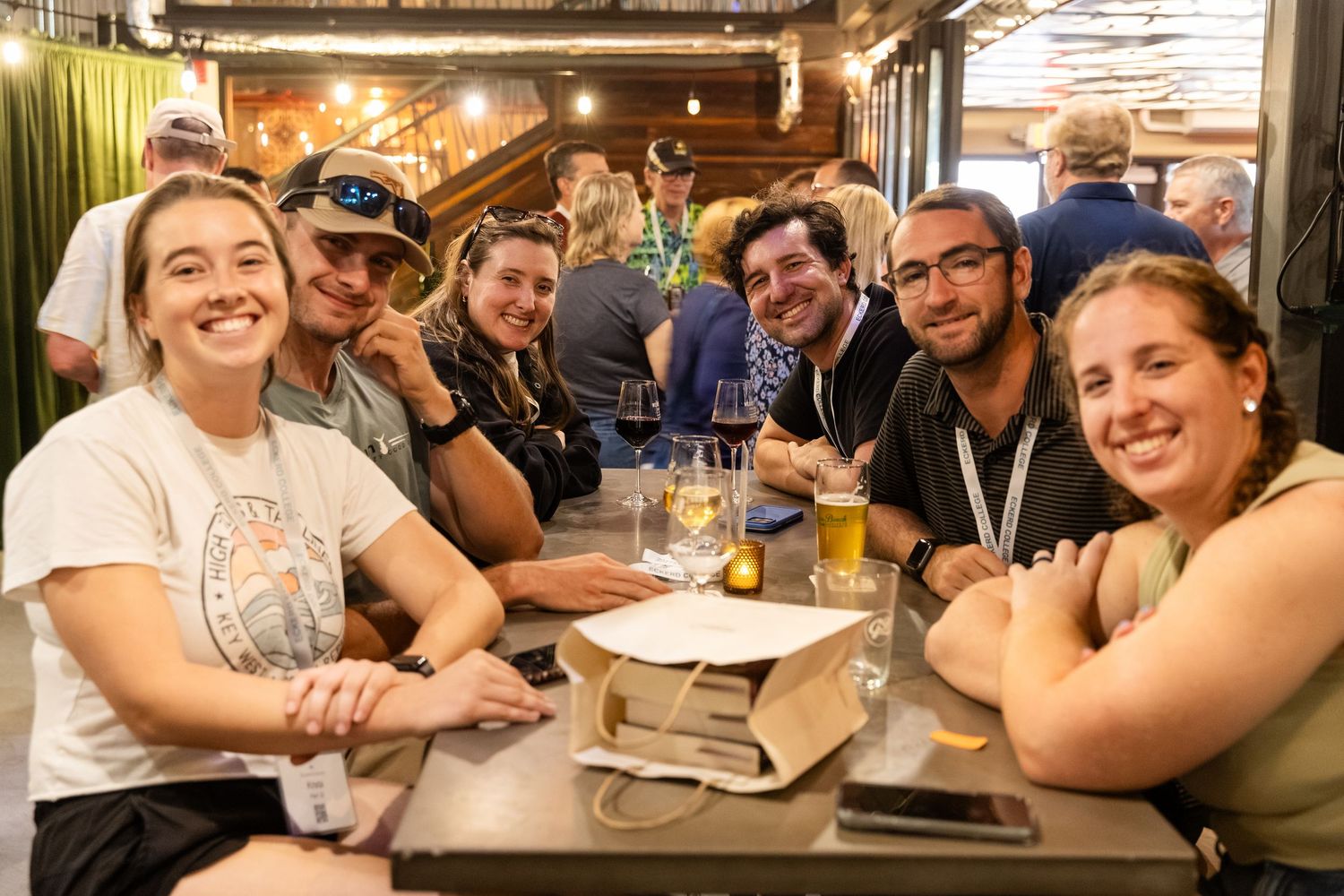 Group of six smiling friends enjoying drinks together at a restaurant table.