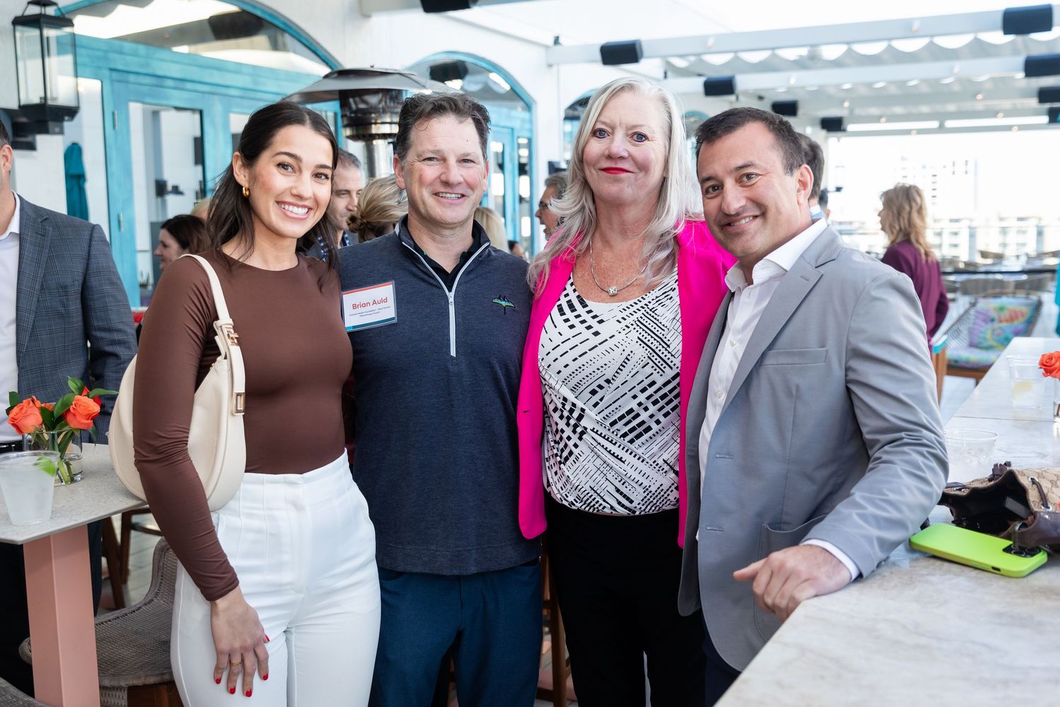 Four smiling professionals posing together at an indoor networking event with floral centerpieces.