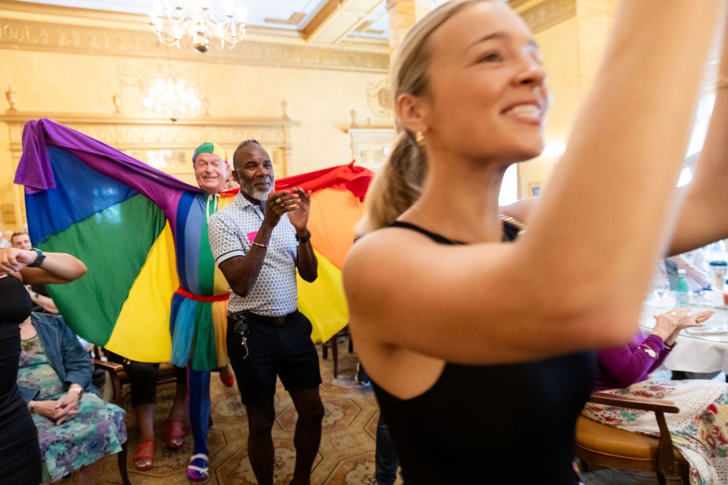 Smiling woman dancing with man holding rainbow Pride flag at a vibrant indoor celebration event.